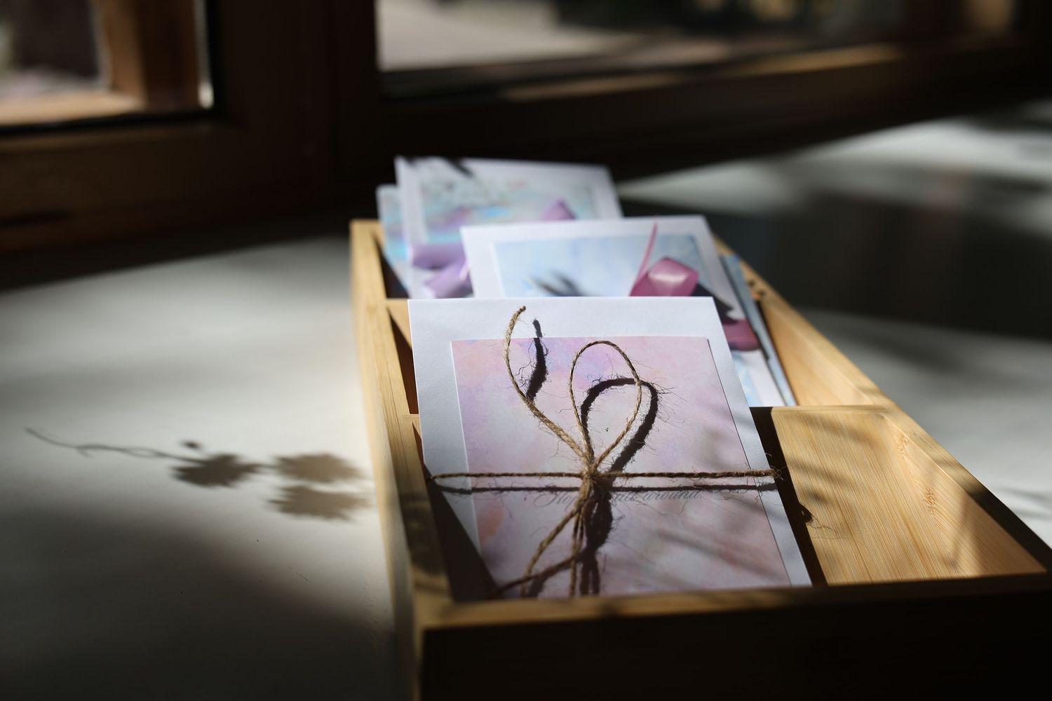 Wooden box filled with greeting cards tied with twine string bows, displayed on a sunlit surface.