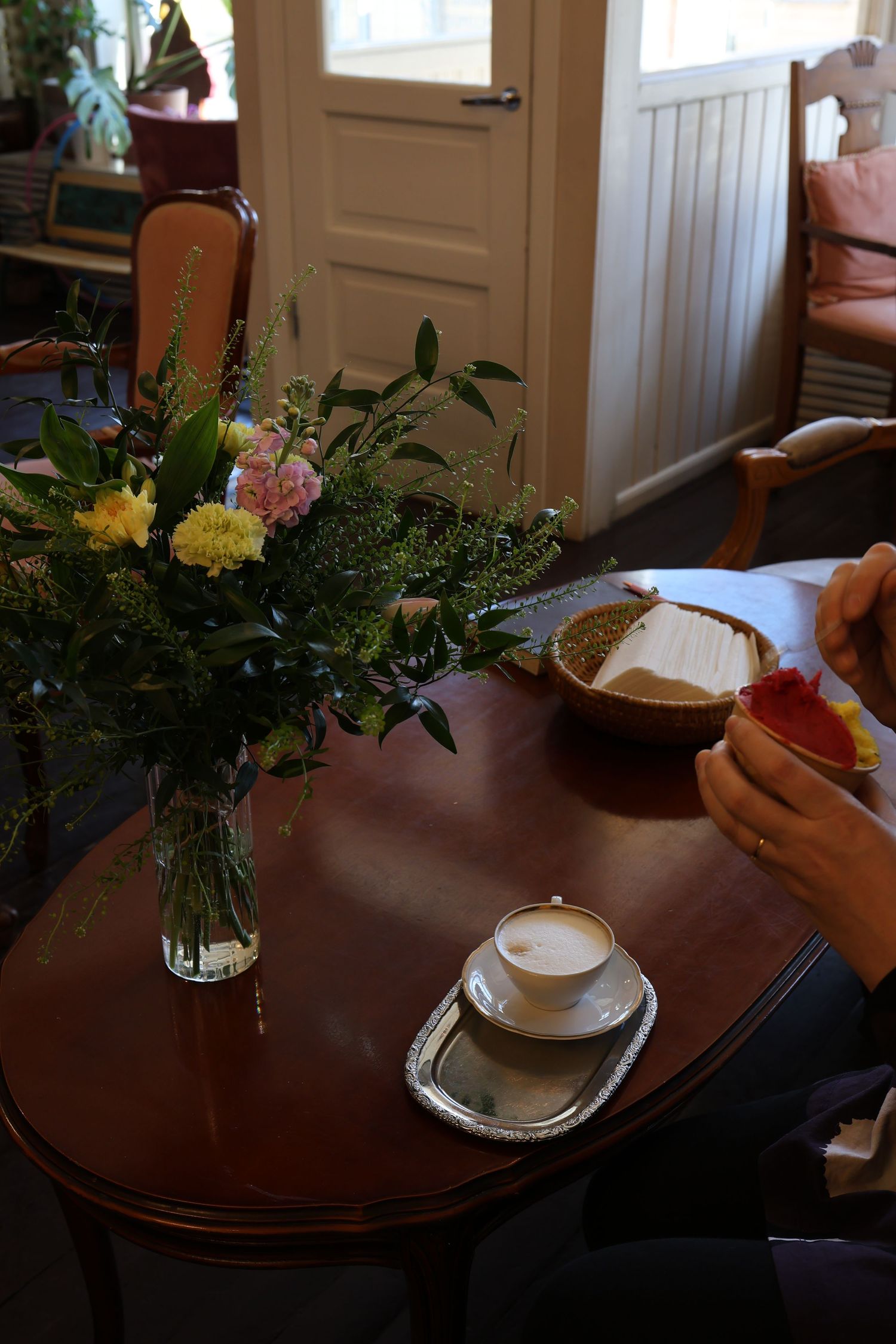 A series of coffee cups and floral arrangements on a dark wooden table in a cozy cafe setting.