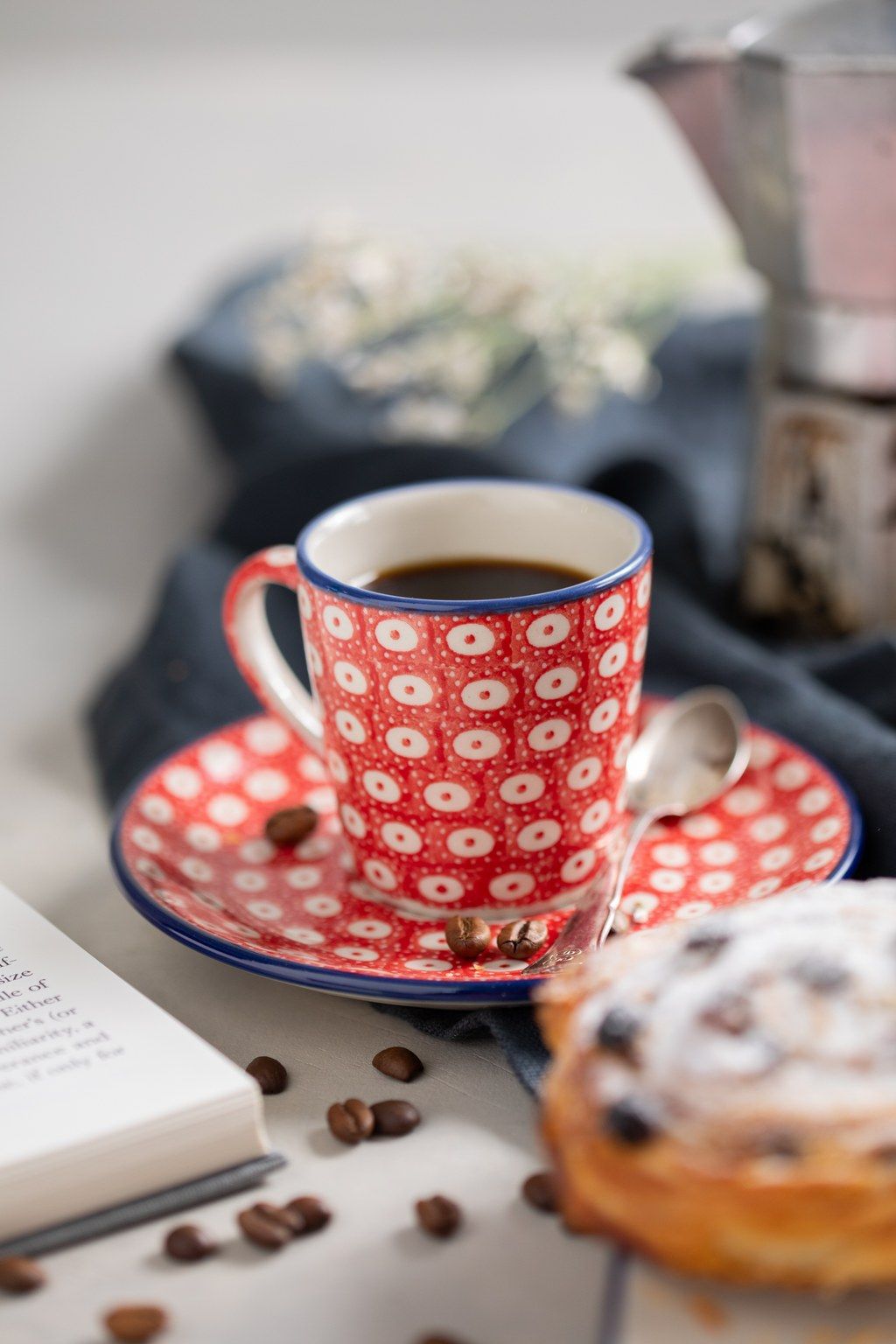 Red and white polka dot teacup and saucer with coffee beans scattered on a light surface creates a cozy scene.
