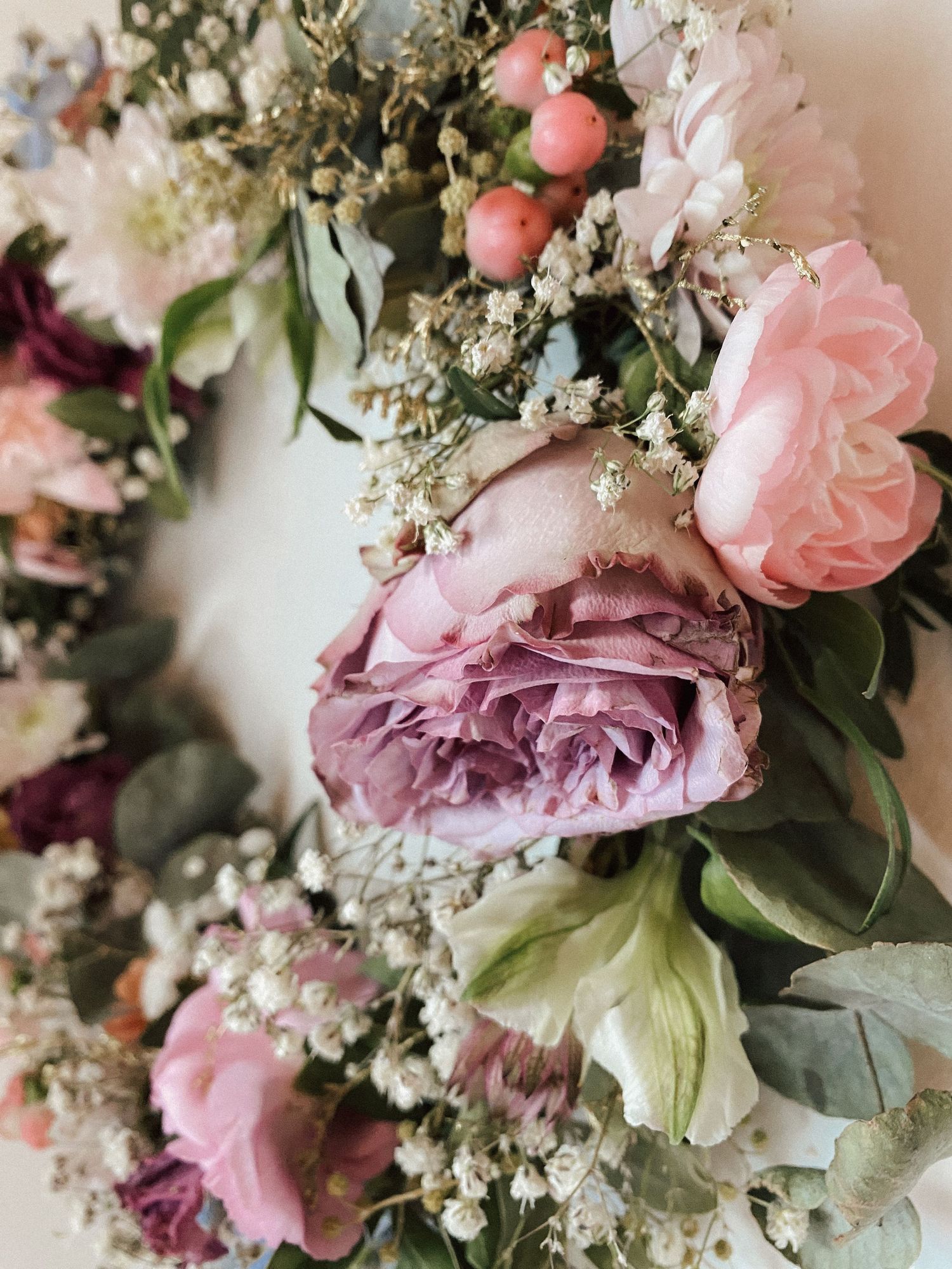 Close-up of a elegant floral wreath featuring pink peonies, roses, berries, and baby's breath in soft pastel tones.