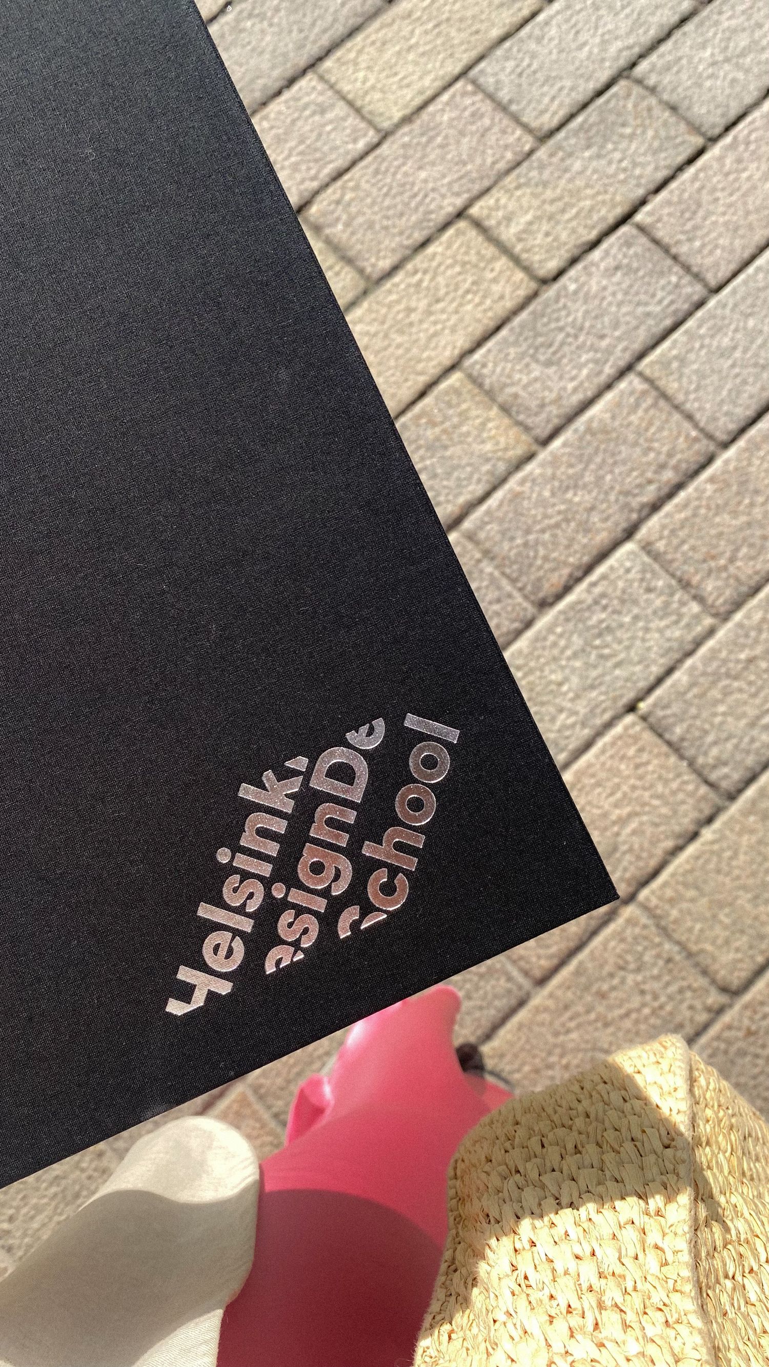 Black printed material with helsinki summer school text visible against beige brick or tile background.