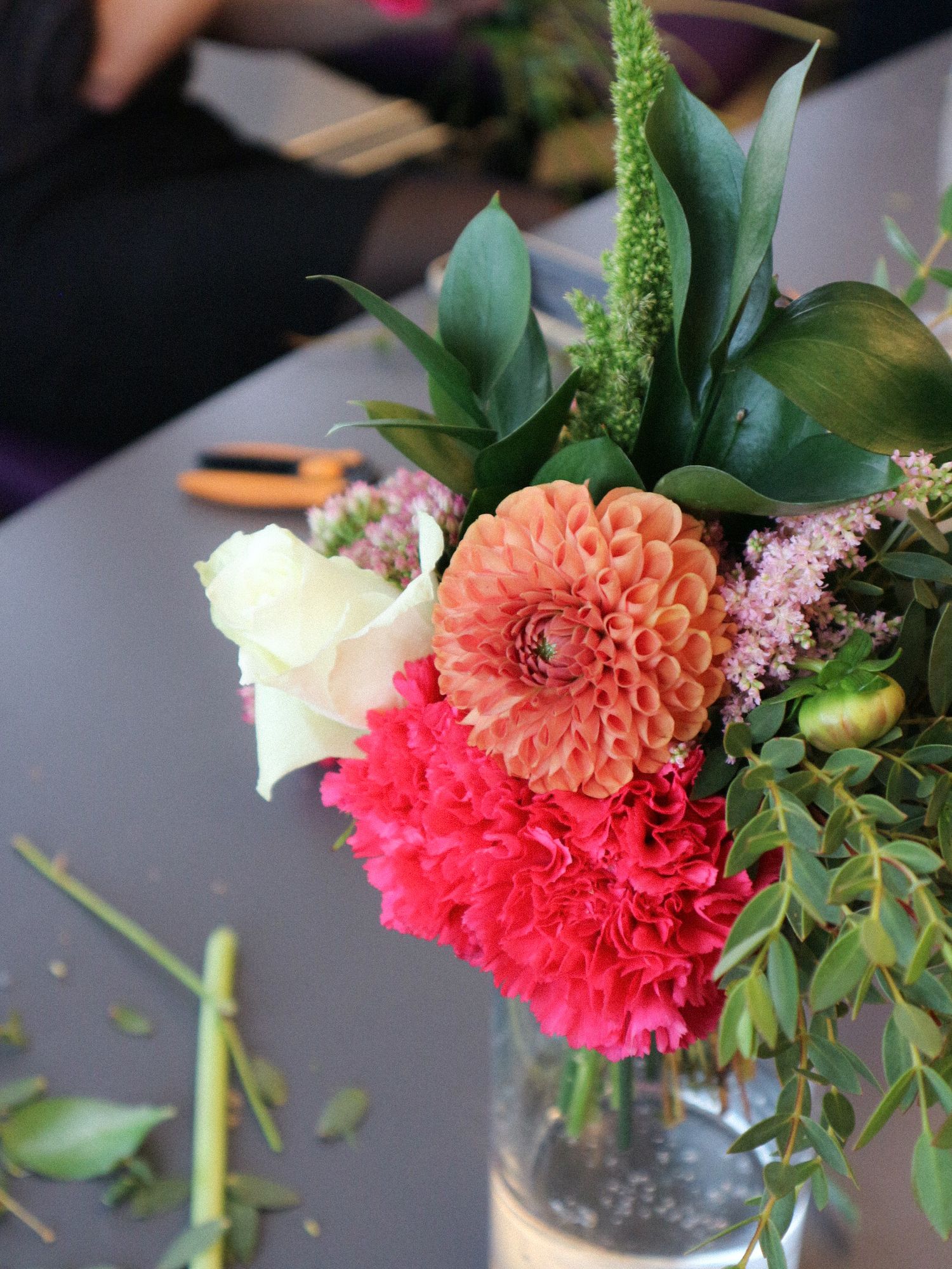 A series of floral arrangements featuring coral dahlias and pink flowers in glass vases against a dark background.