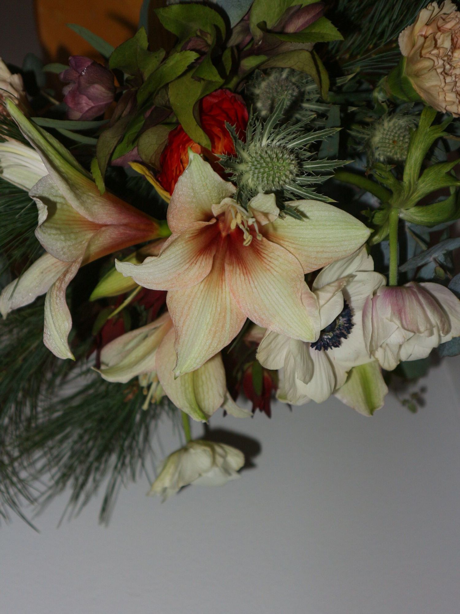 A festive floral arrangement featuring lilies, roses, and evergreen branches in soft peach and red tones.