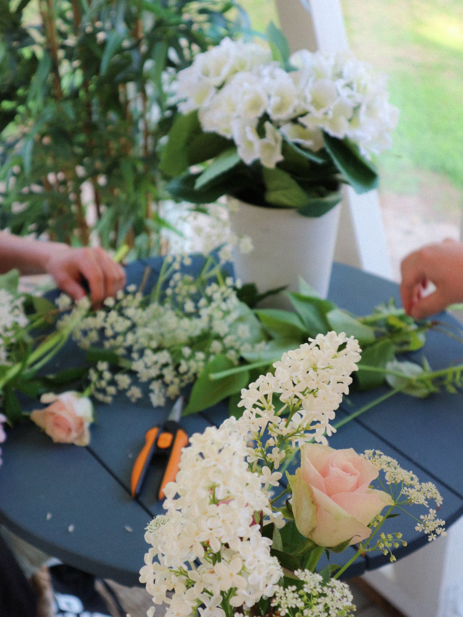 Arraying white and pink flowers with greenery across a dark blue surface while trimming and arranging floral elements.