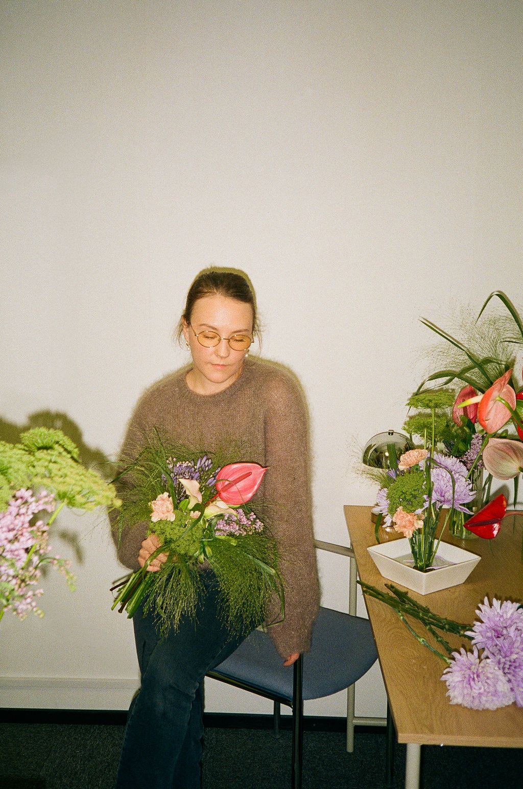 Person in brown sweater arranges colorful flowers and greenery in artistic floral composition series.