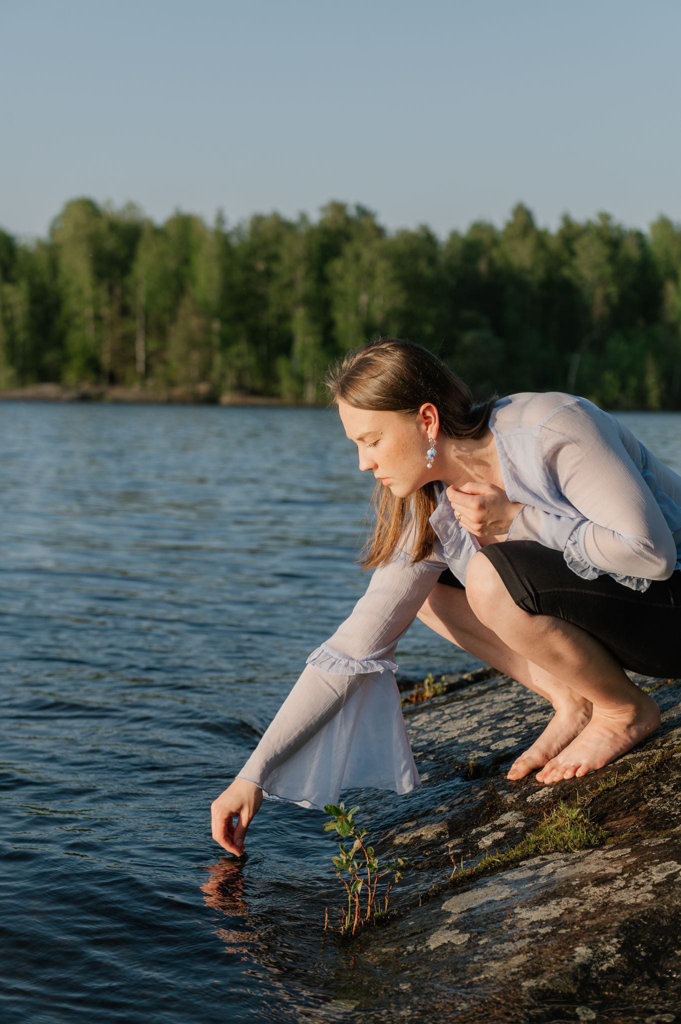 Four images in sequence show a person in a white sweater leaning out over the water from rocky lakeside during sunset.