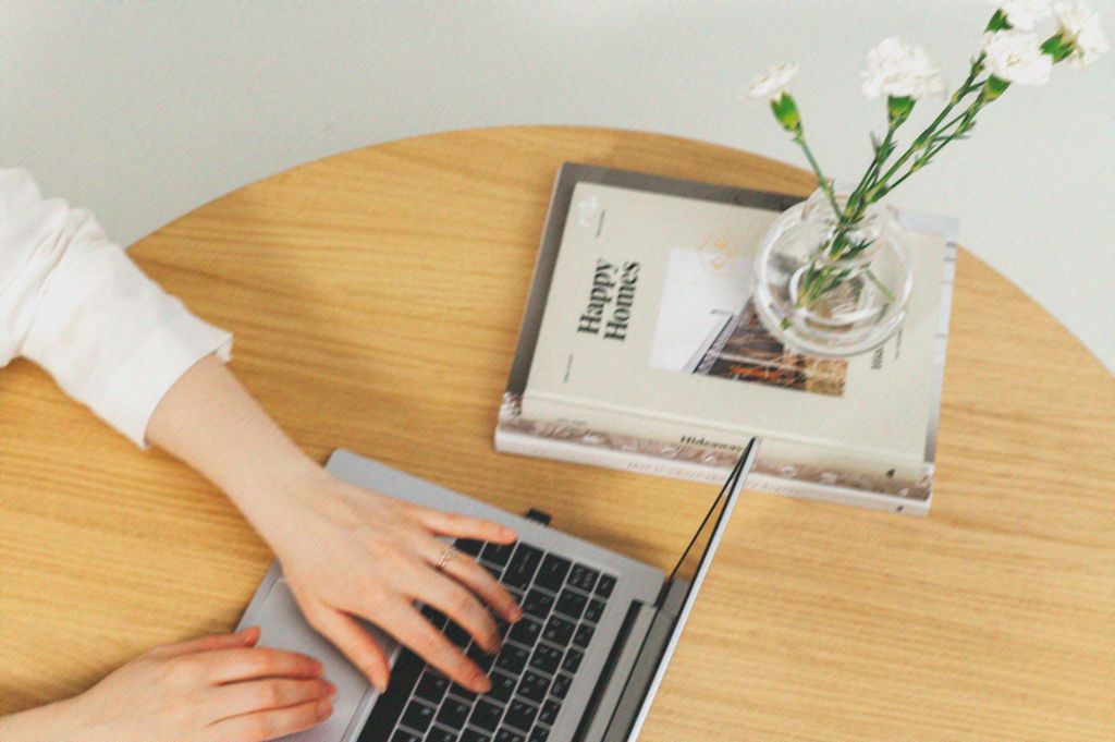 Person working at wooden desk with laptop and small green plant in minimalist workspace setting.