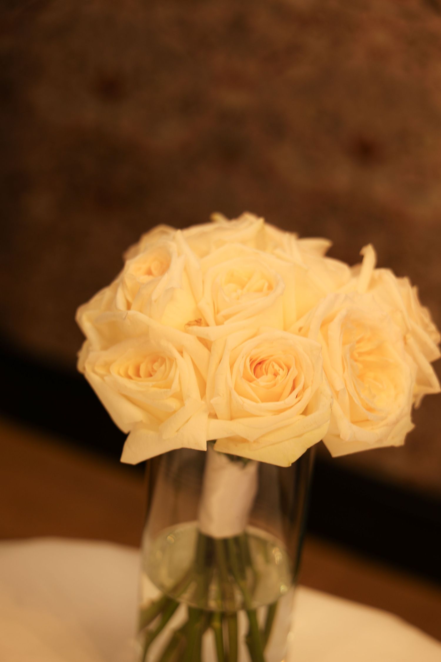 A bouquet of cream white roses arranged in a clear glass vase on a white table.
