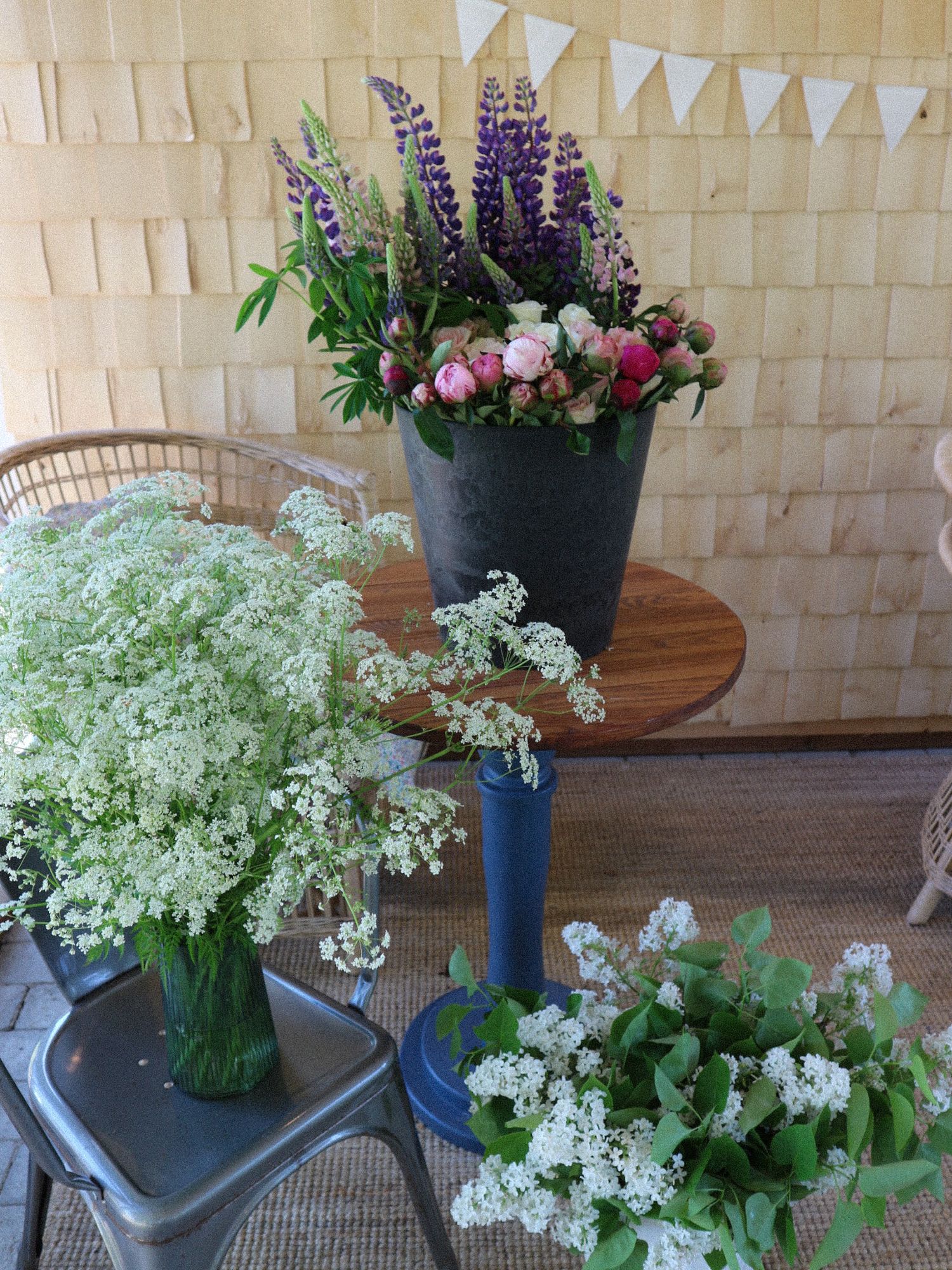 Fresh floral arrangement featuring purple lupines, pink peonies, and white baby's breath displayed on wooden tables with bunting.