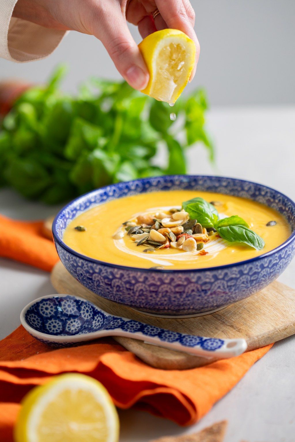 Creamy butternut squash soup garnished with pumpkin seeds and fresh herbs served in blue patterned bowls with lemon.