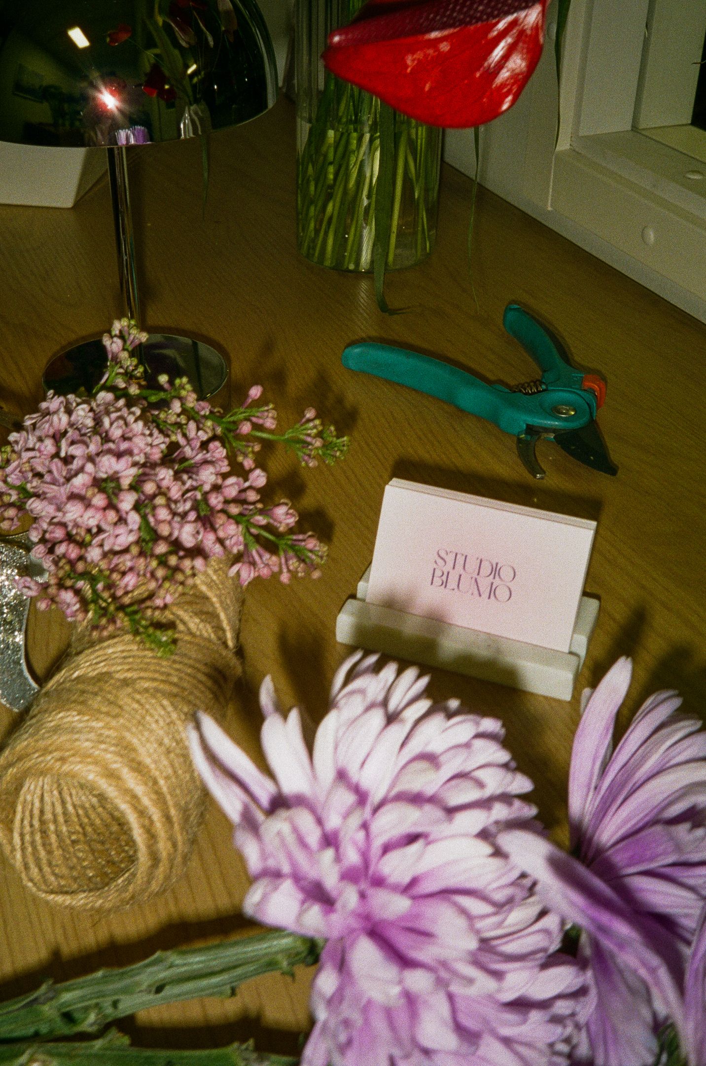 Floral studio workspace with pink flowers, pruning shears, and Studio Bremo business cards on a wooden surface.