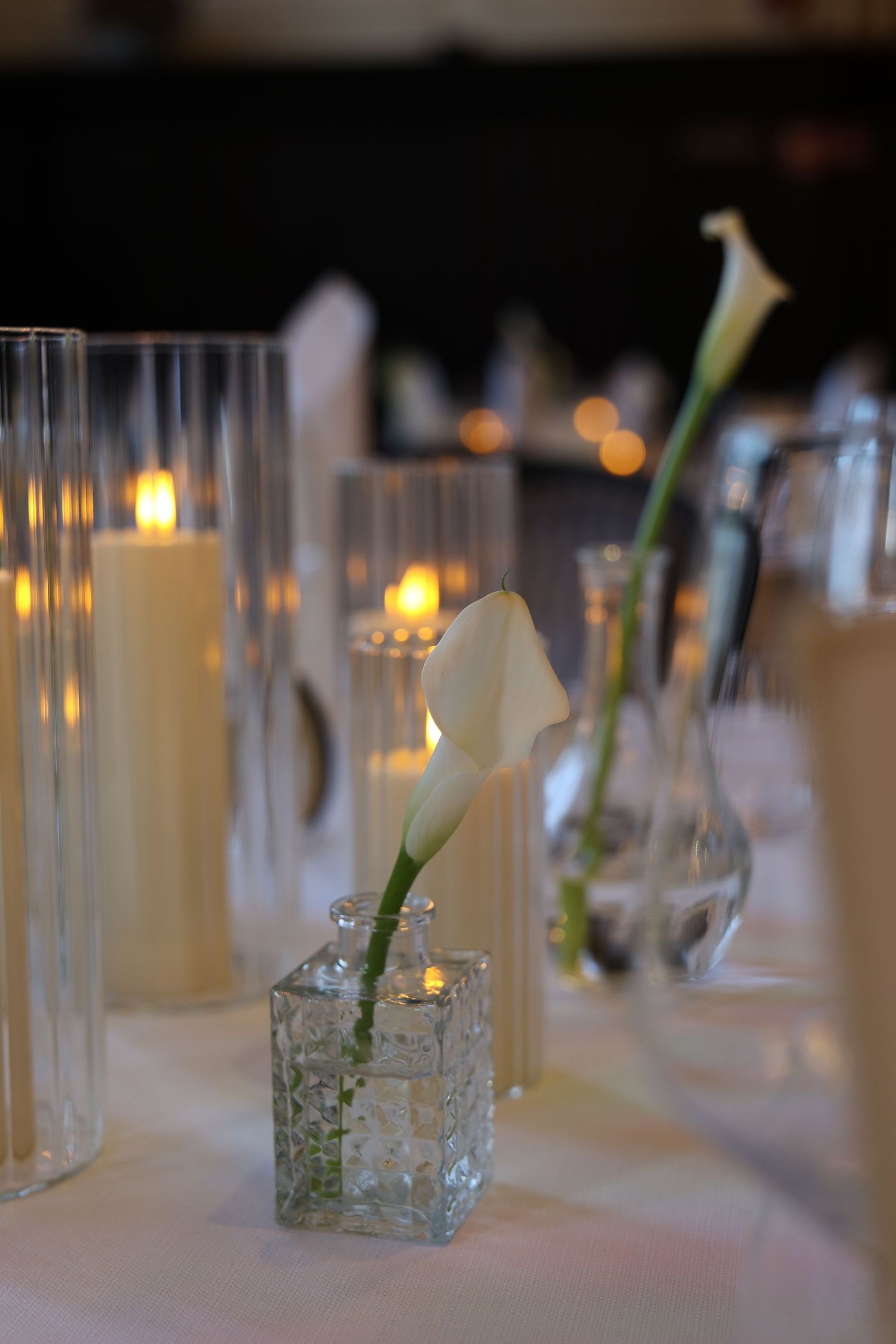Glass votive candle holders with single stems create an elegant table centerpiece at an evening event.