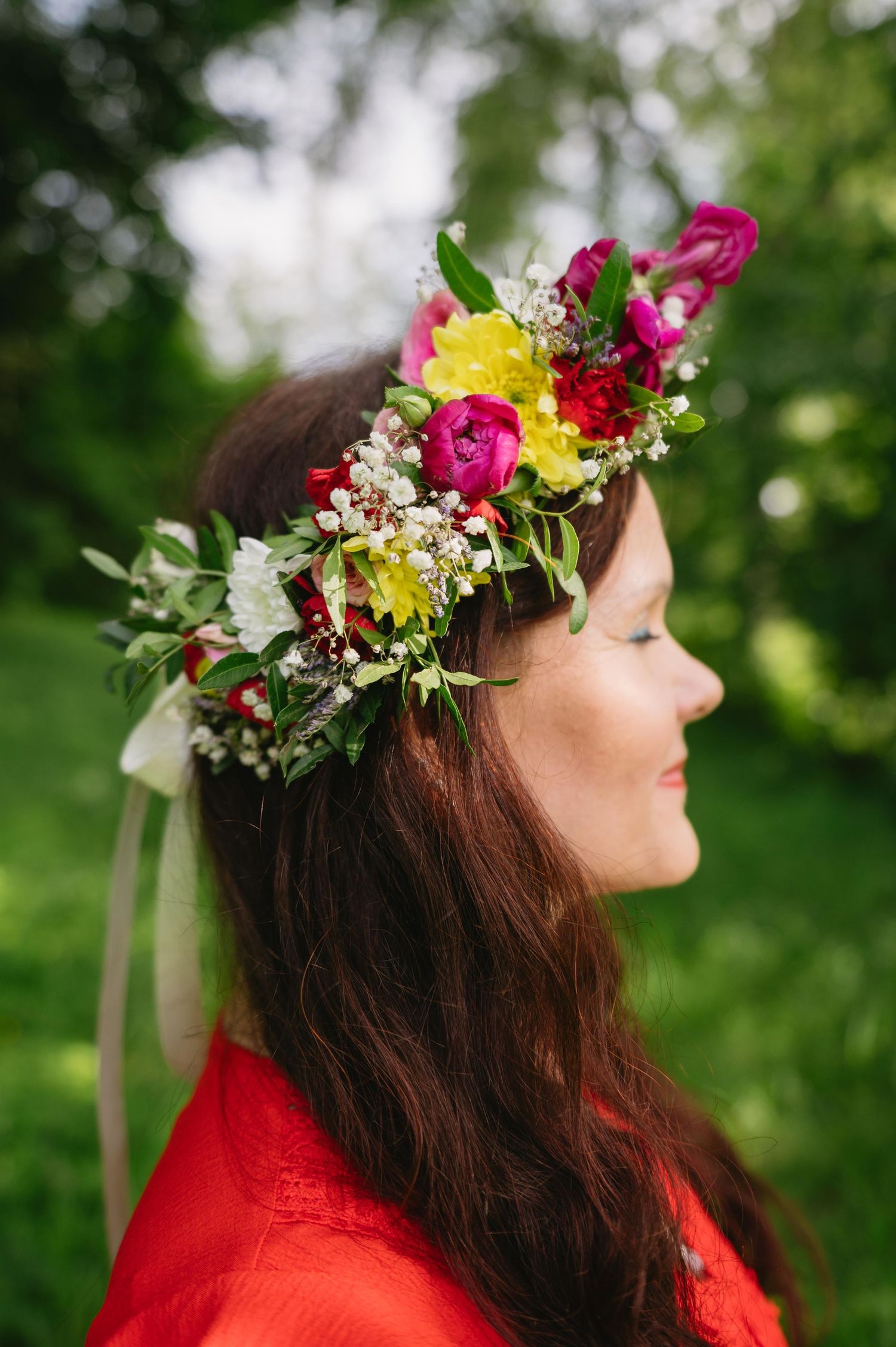 Profile of someone wearing a vibrant flower crown with pink and yellow blooms against a soft green garden background.