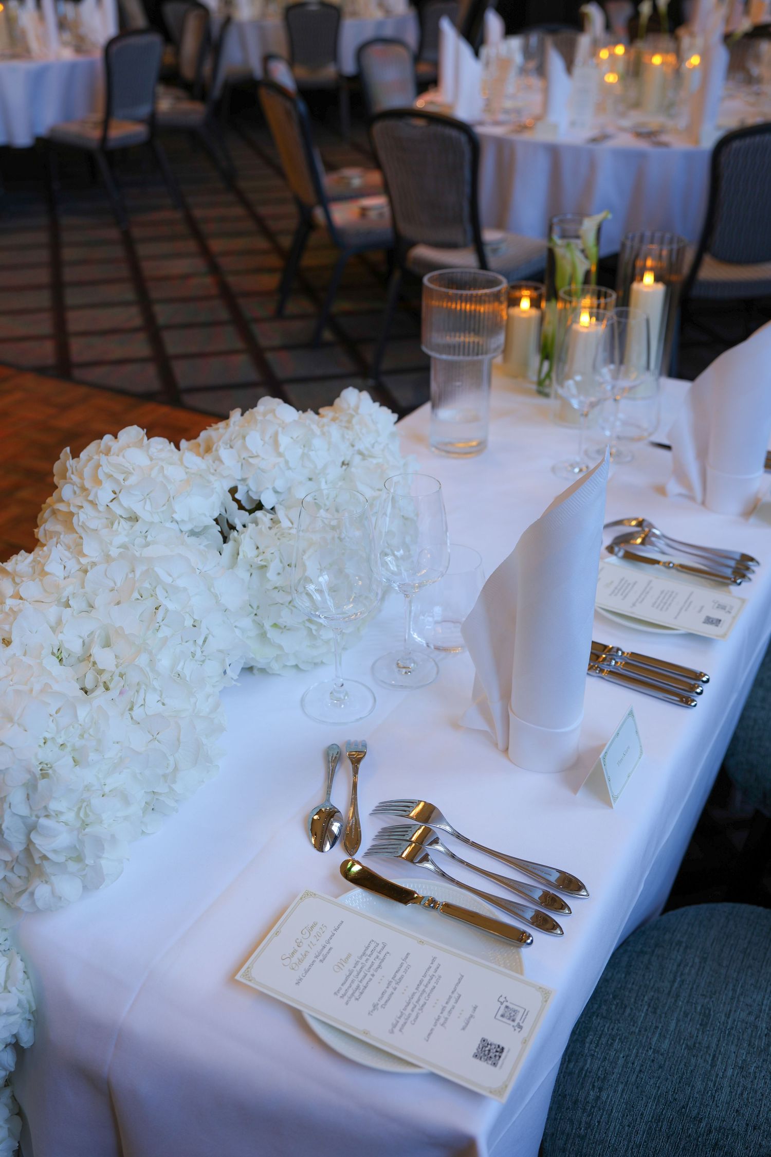Elegant white table settings with floral centerpieces and menu cards at a formal wedding reception.