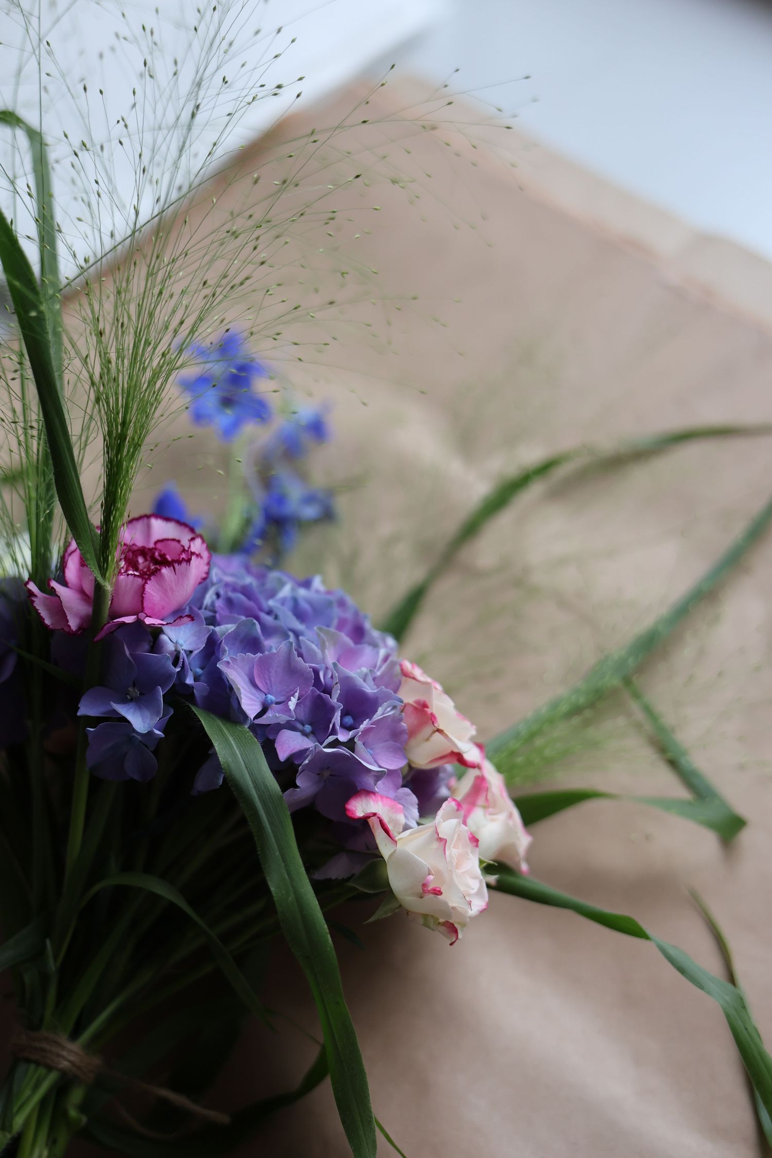 A rustic bouquet of purple hydrangeas, pink roses, and blue flowers wrapped in kraft paper.