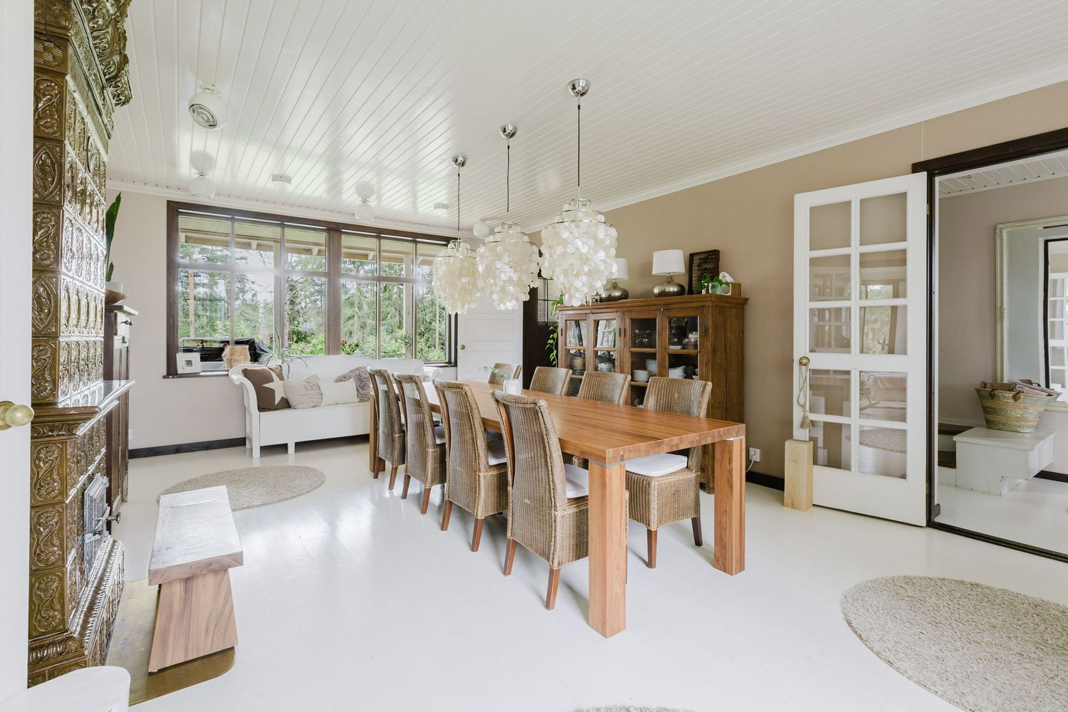 Modern dining room with wooden table, upholstered chairs, white pendant lights and French doors leading to living area.
