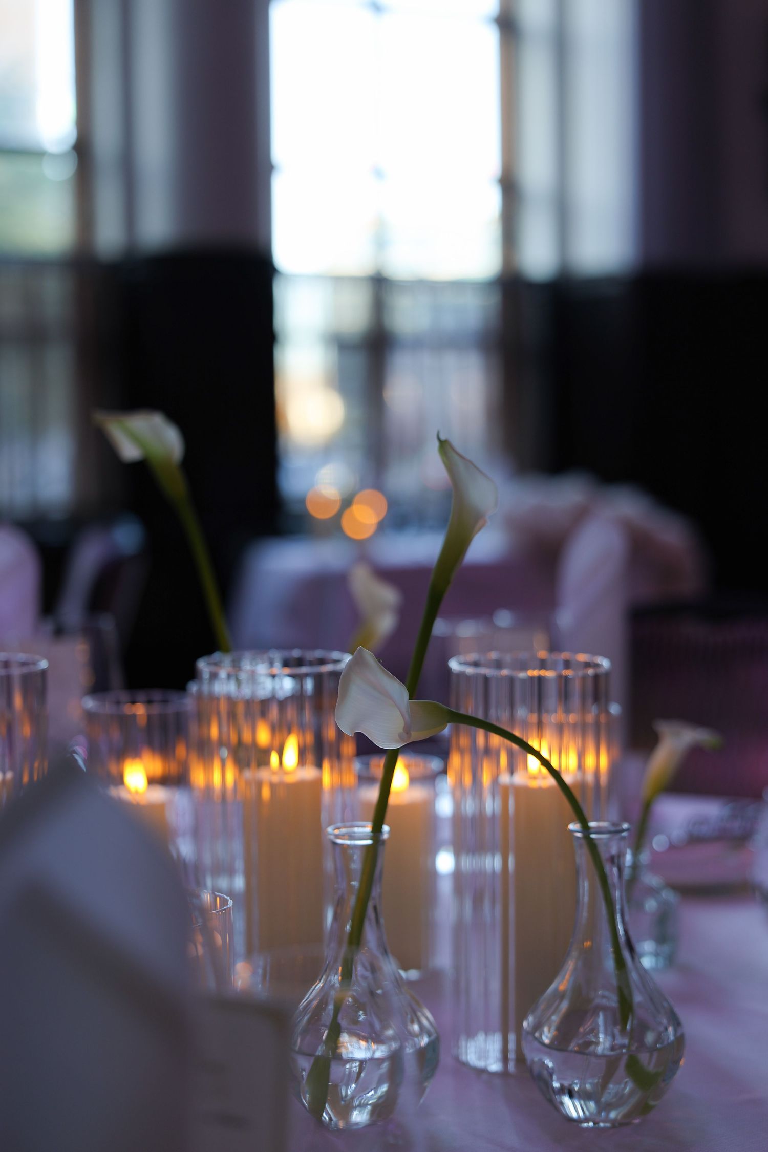 Glass vases with lit candles and floral decorations create an elegant table setting at a formal event.
