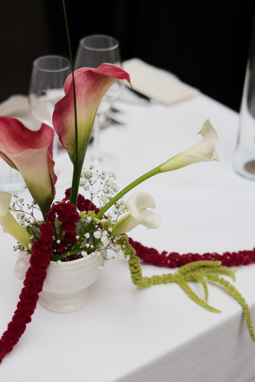 Elegant wedding table centerpiece with pink and white calla lilies, baby's breath, and red amaranthus in a white vase.