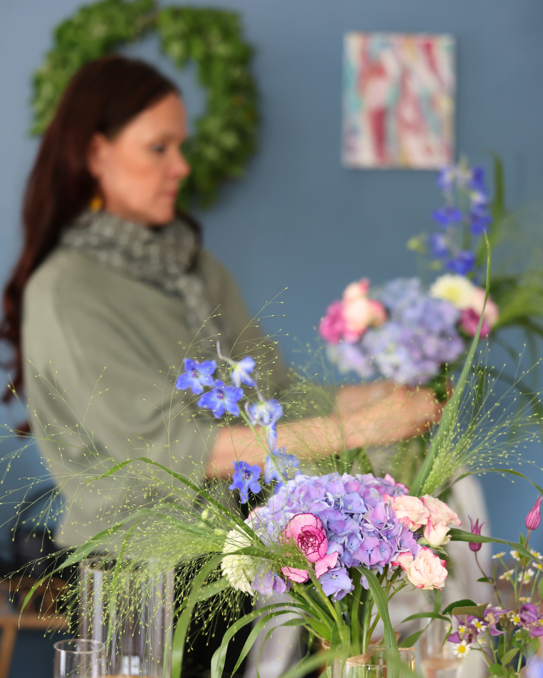 Florist arranging colorful flower bouquets with hydrangeas and roses on a table in a blue studio.