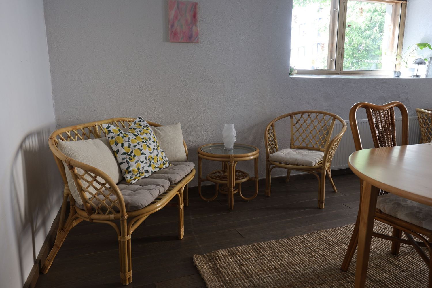 Cozy rattan sofa and chairs with cushions around a small coffee table in a bright, minimalist living room.