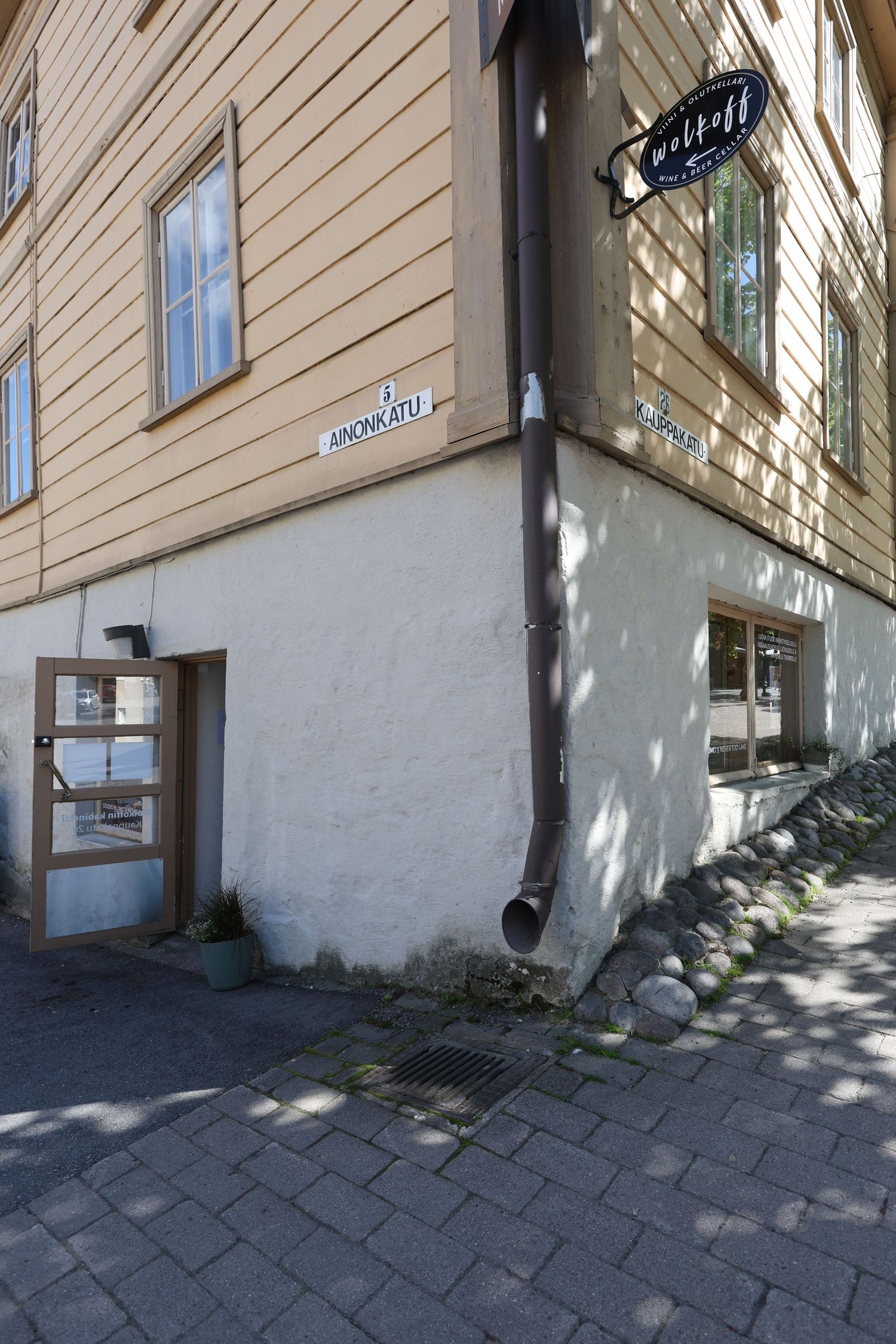 Corner of a historic wooden building with white plaster base, drainpipe, and street signs on cobblestone pavement.