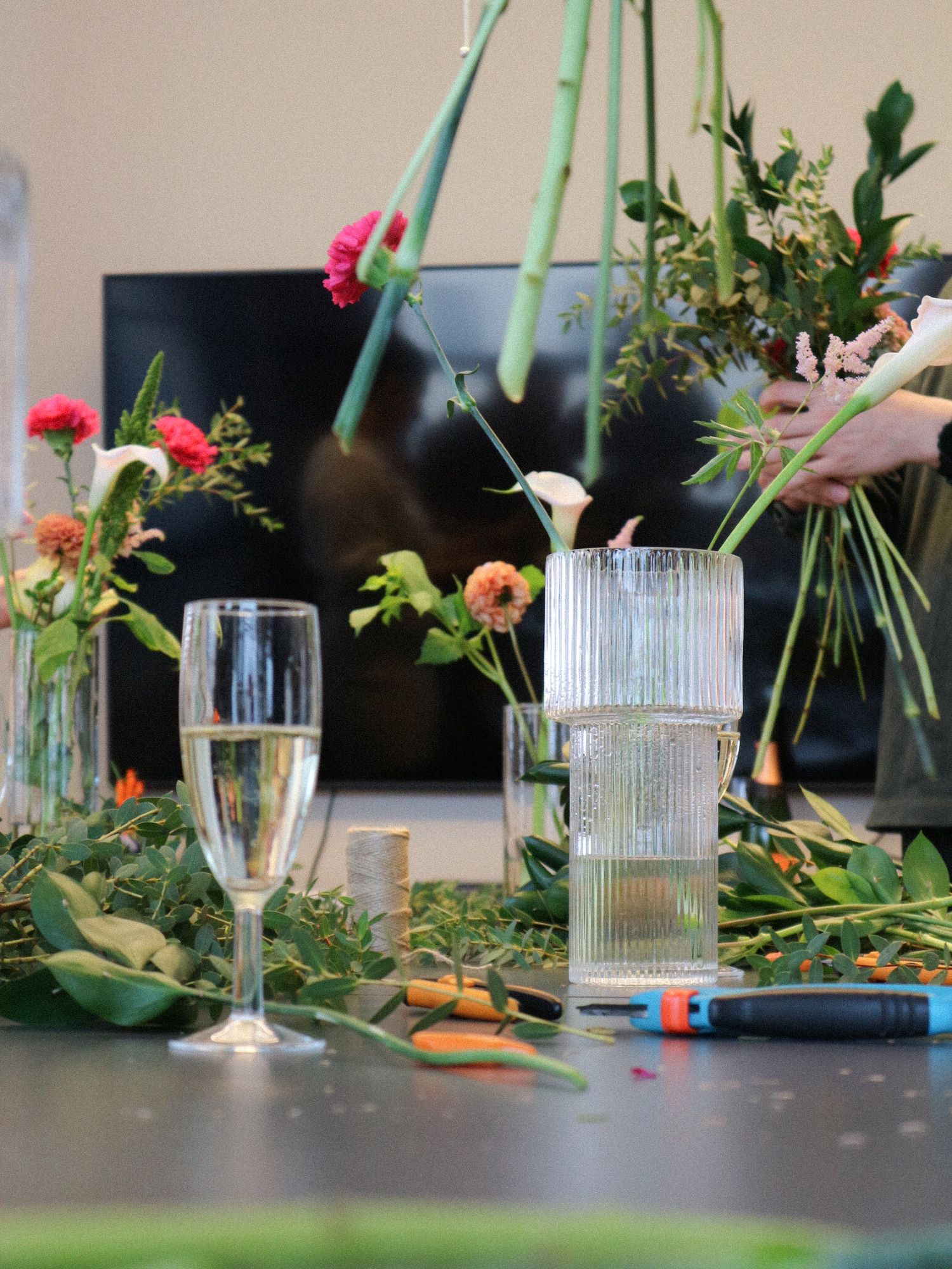 A floral arrangement workshop setup with champagne glass, clear vases, and scattered flowers on a gray surface.