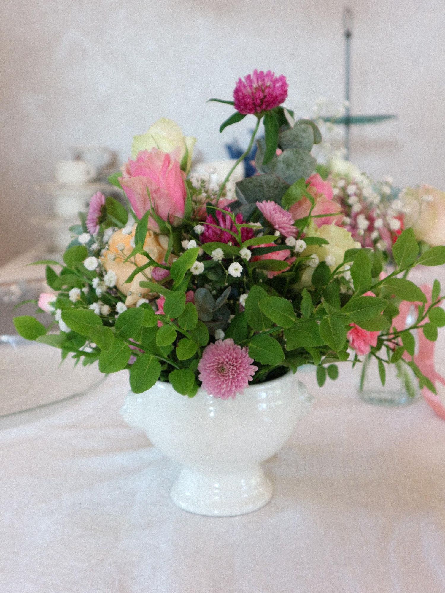 A delicate floral arrangement featuring pink chrysanthemums and white baby's breath in a low white ceramic bowl.