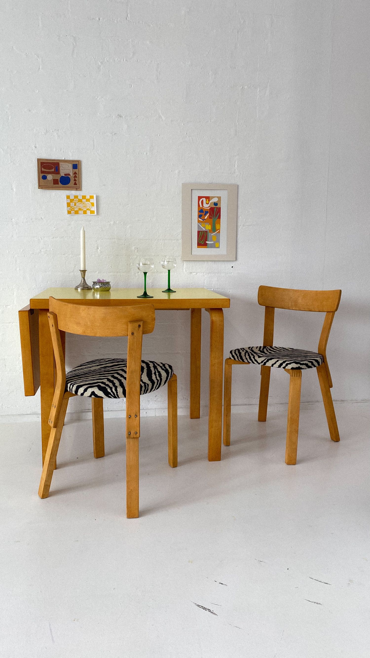 Vintage wooden drop-leaf dining table with zebra print upholstered chairs and small framed artwork on white wall.