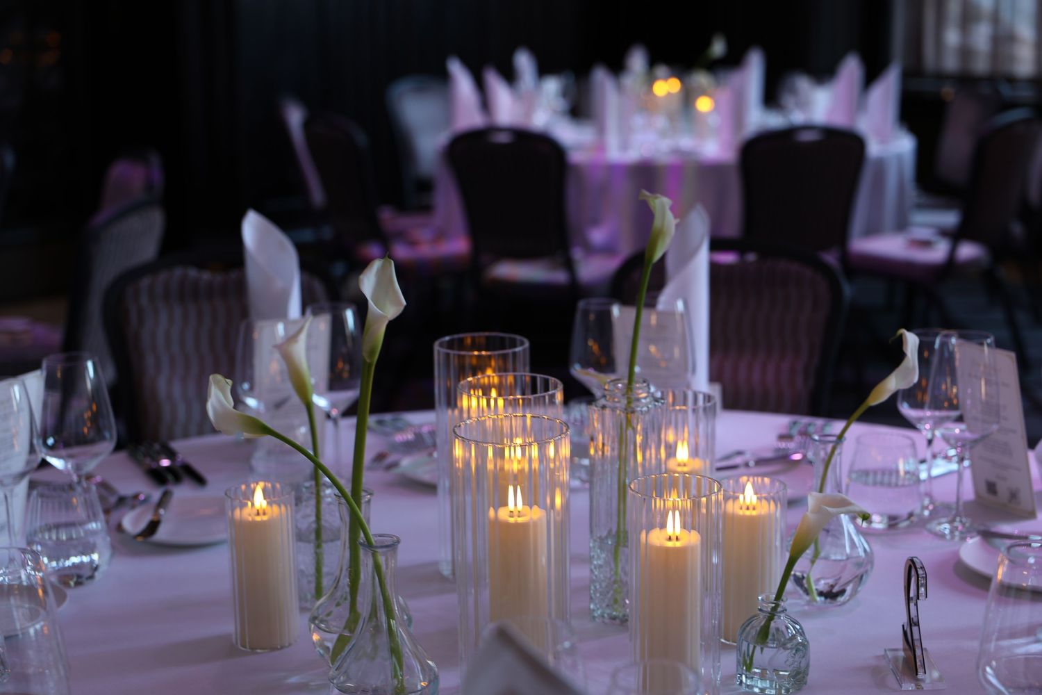 Elegant wedding reception tables decorated with glowing candles and white floral centerpieces in a dimly lit venue.