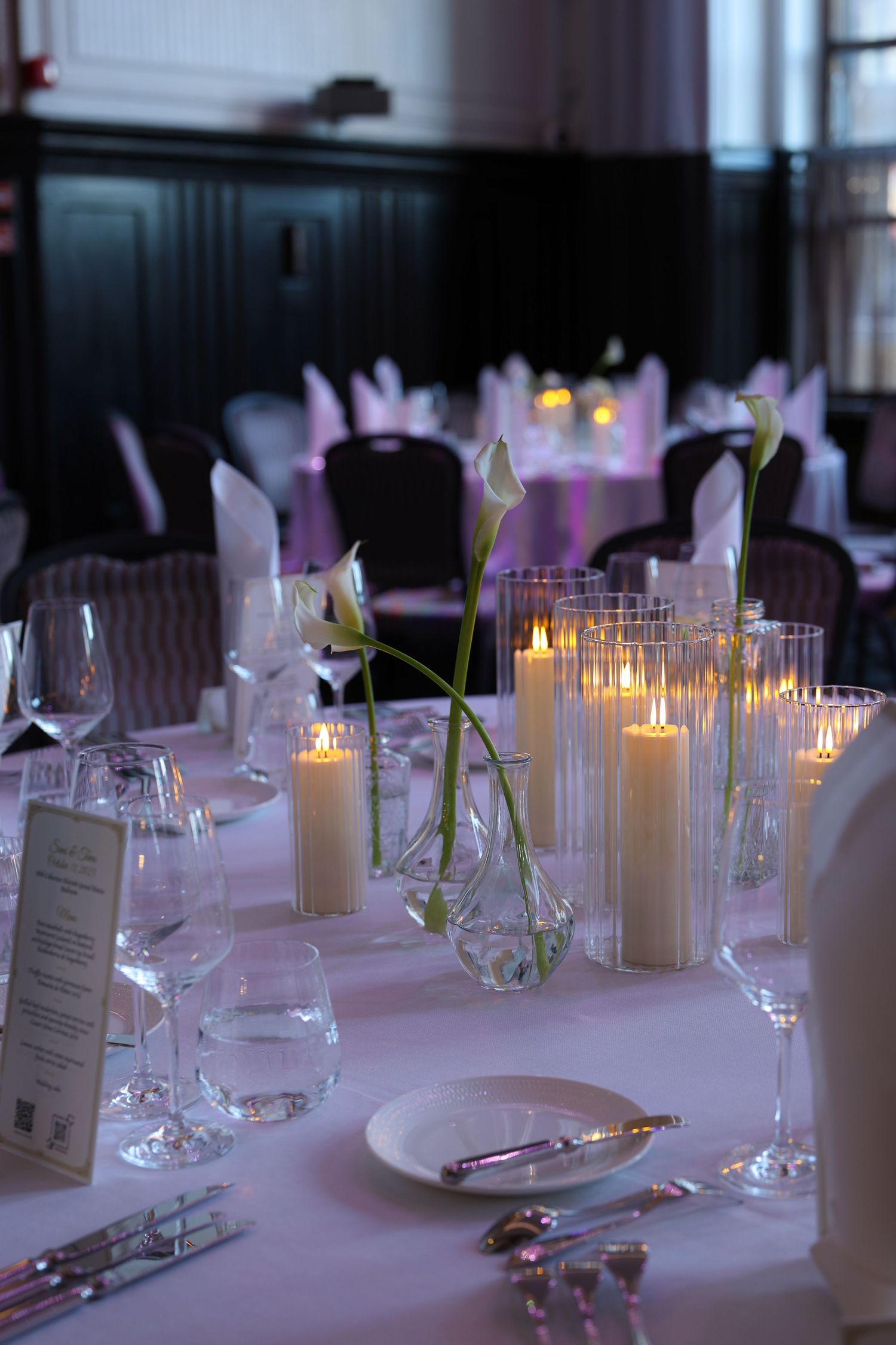 Elegant table setting with white linens, glowing candles, and wine glasses creating a romantic dining atmosphere.