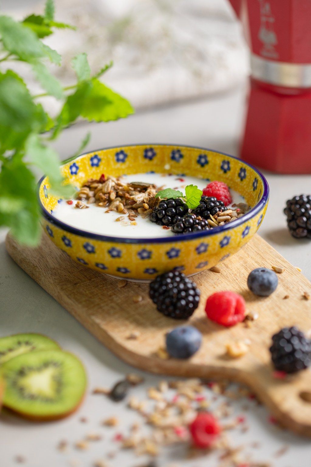 A decorative ceramic bowl with blue and white pattern holds fresh berries and granola on a wooden serving board.