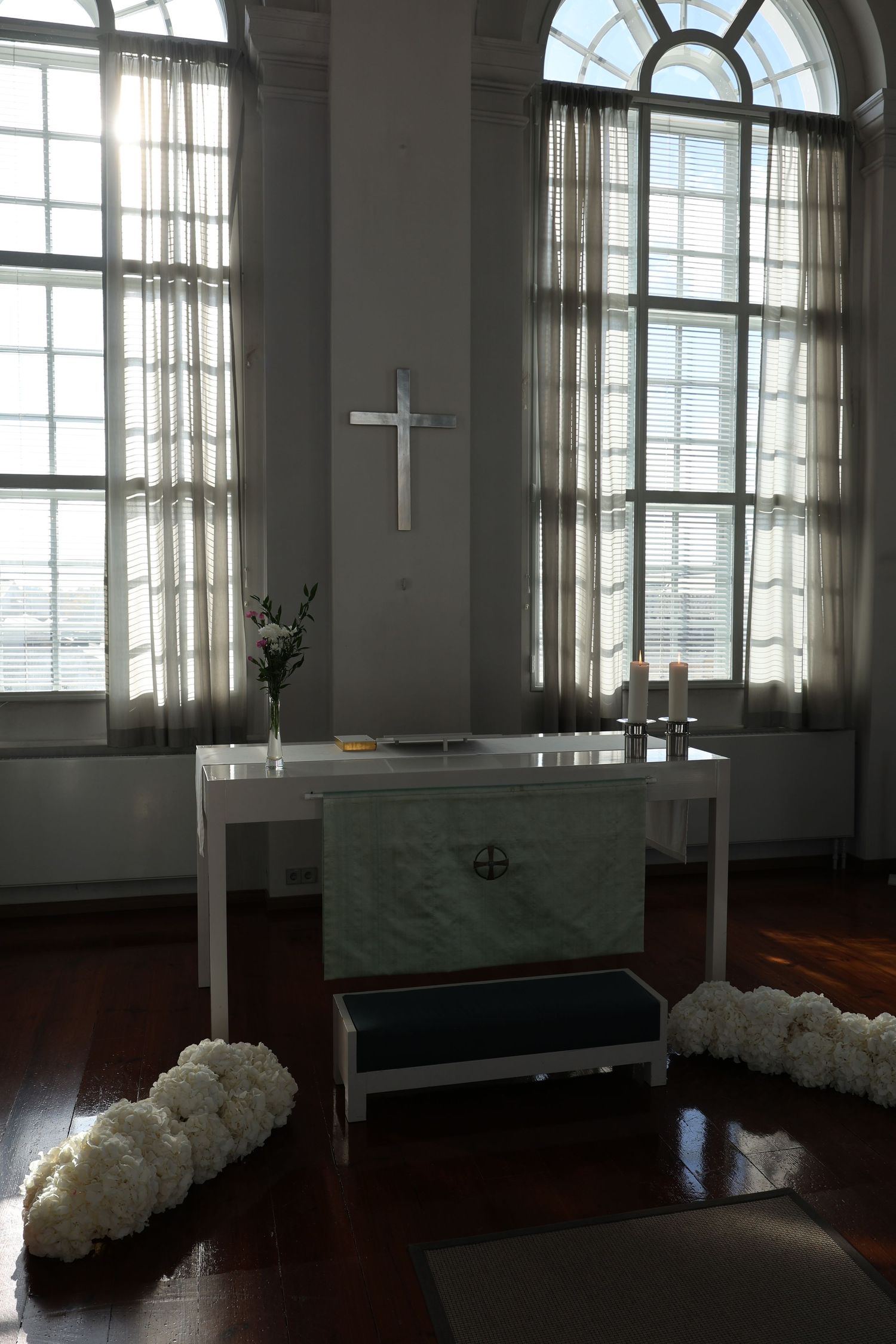 Sunlight streams through tall windows in a minimalist room with white walls and dark hardwood floors.