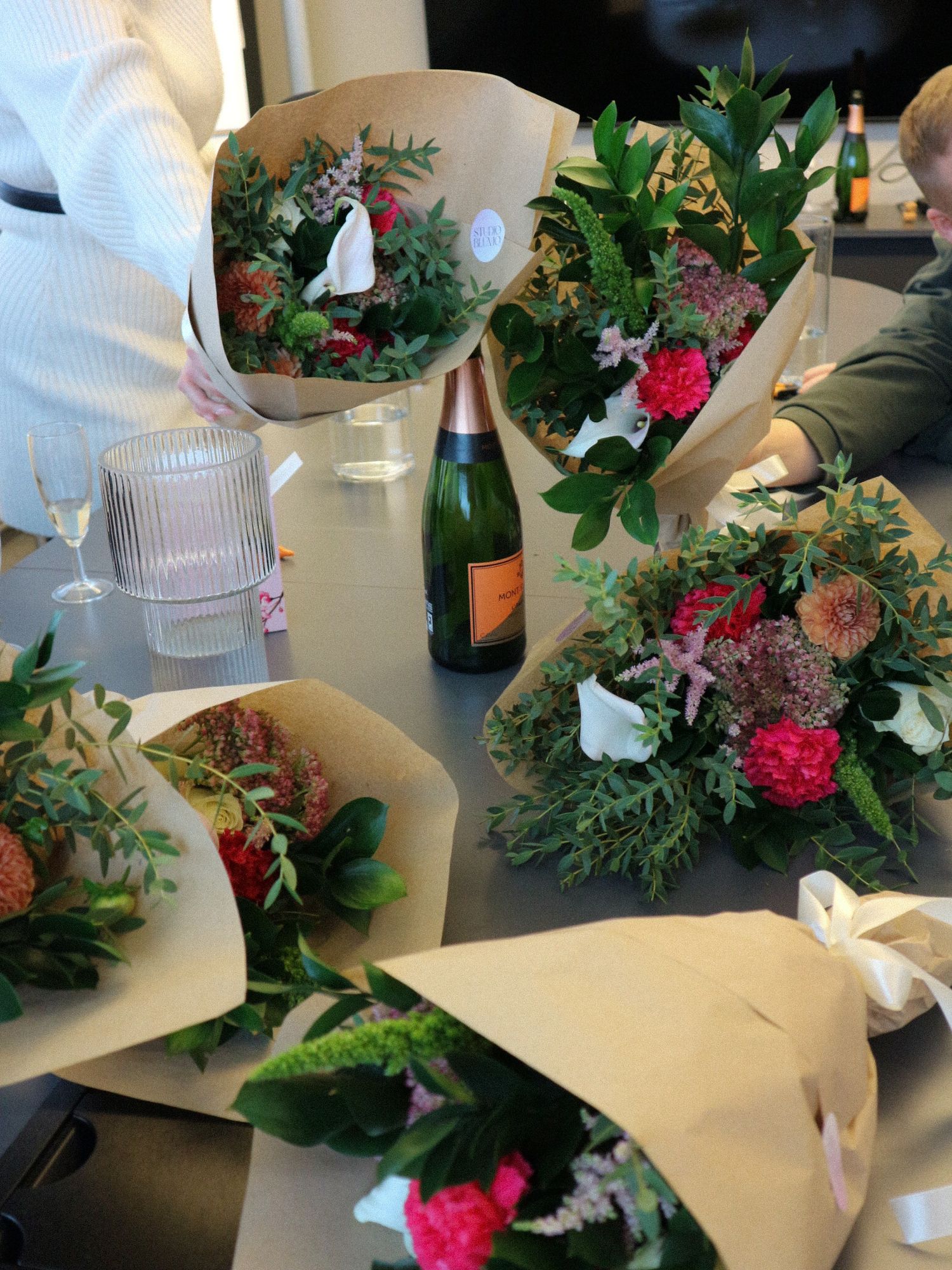 Several wrapped floral arrangements with pink flowers and greenery are displayed on a light-colored surface.