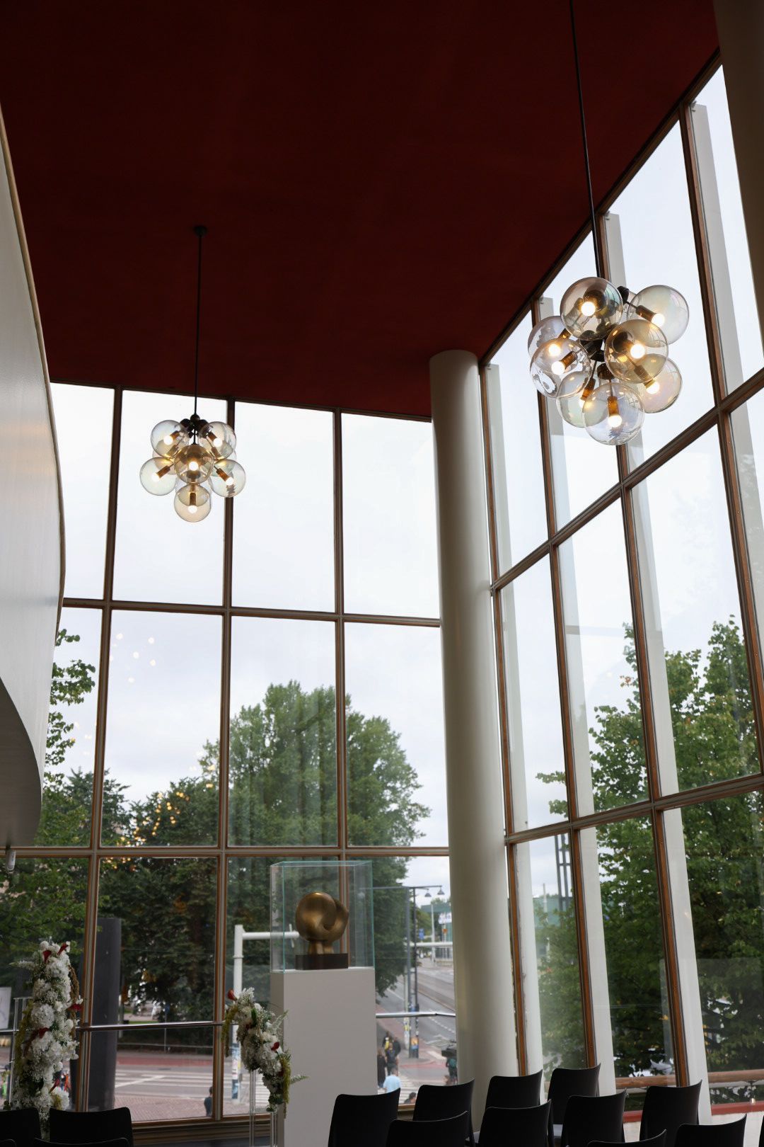 Modern interior with cluster pendant lights and floor-to-ceiling windows overlooking green trees.
