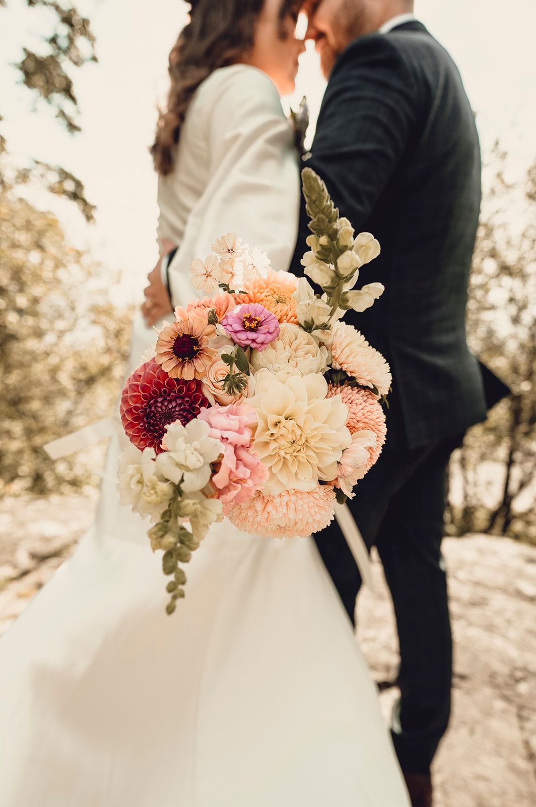 A stunning bridal bouquet with pink and peach dahlias against a romantic outdoor wedding scene at sunset.