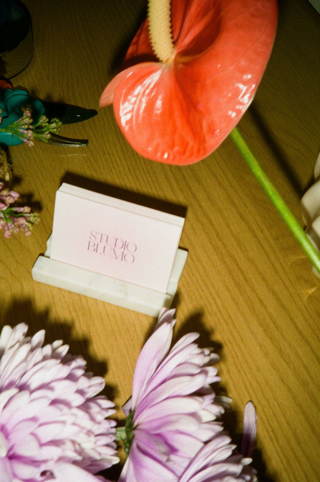 Pink and coral flowers arranged on a wooden surface next to small white cards create an elegant composition.