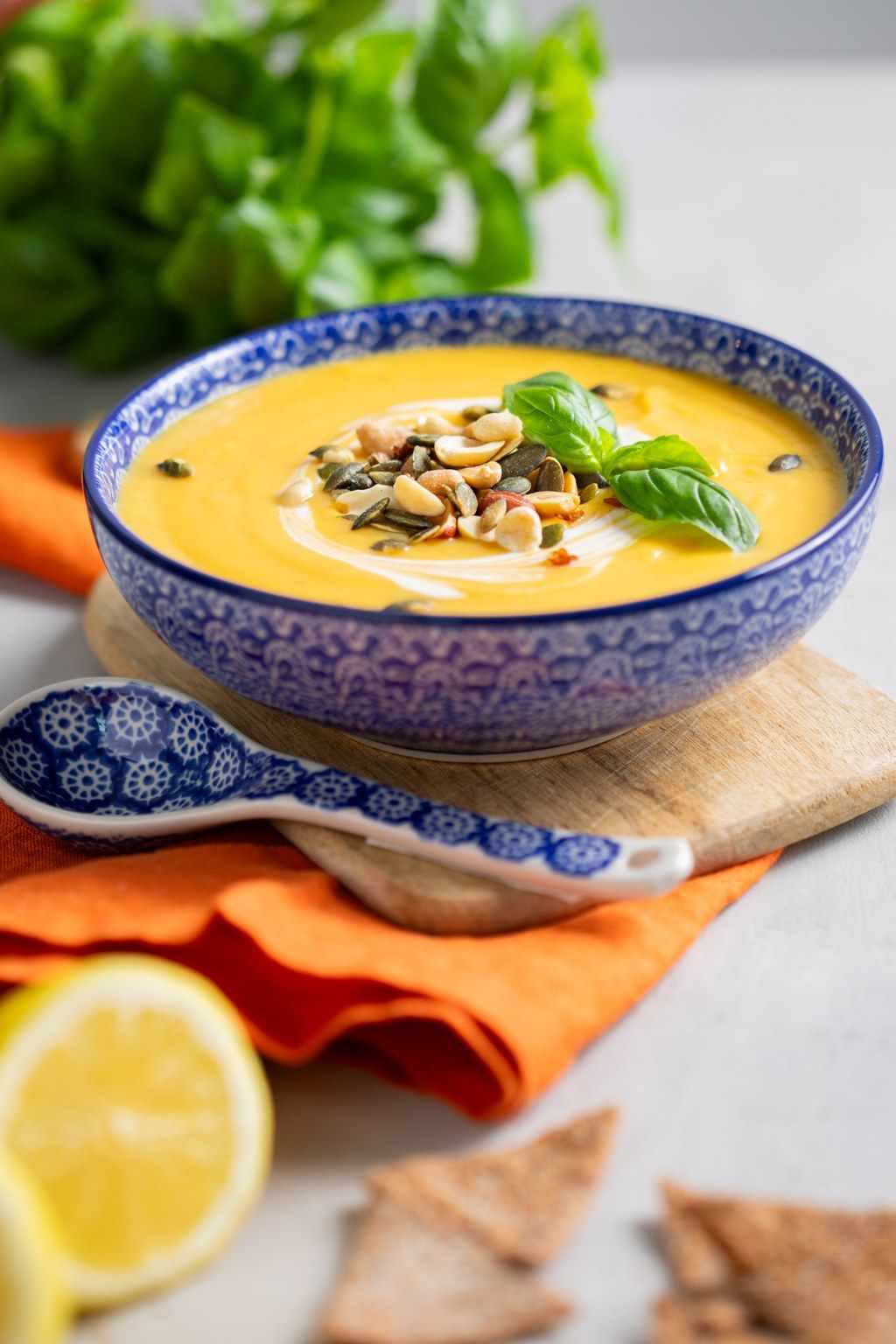 Creamy butternut squash soup topped with pumpkin seeds served in decorative blue bowl with lemon and herbs.