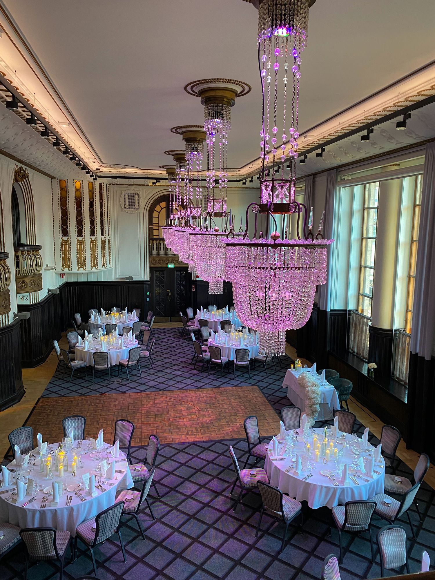 Elegant ballroom setup with round tables, white linens, and purple crystal chandeliers creating a luxurious atmosphere.