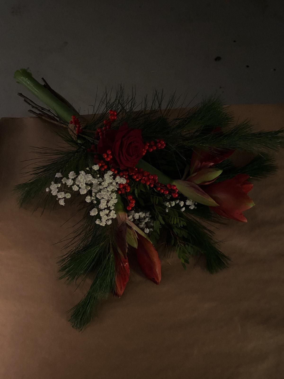 A rustic holiday garland with pine branches, red berries, and delicate white flowers against a dark background.