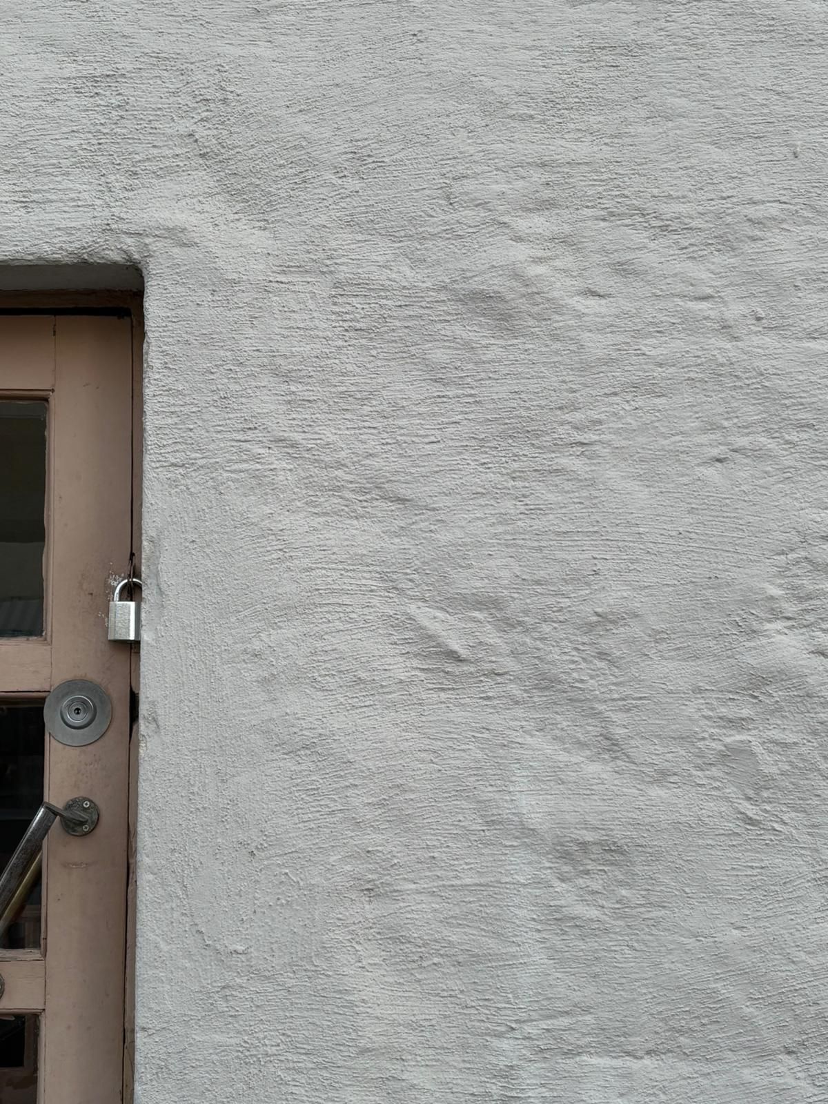 White stucco building exterior with a wooden door secured by a padlock on the left side.