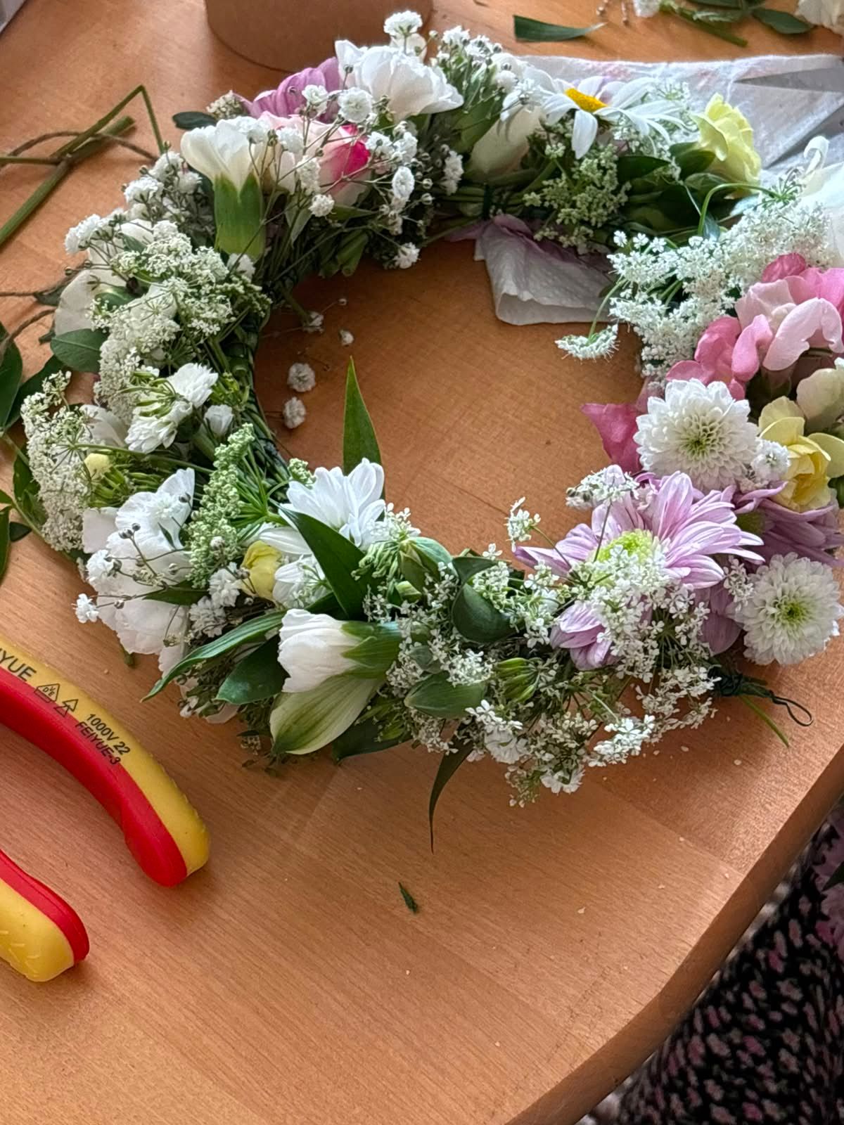 Handmade floral wreath with white daisies, pink flowers, and baby's breath on a wooden table.