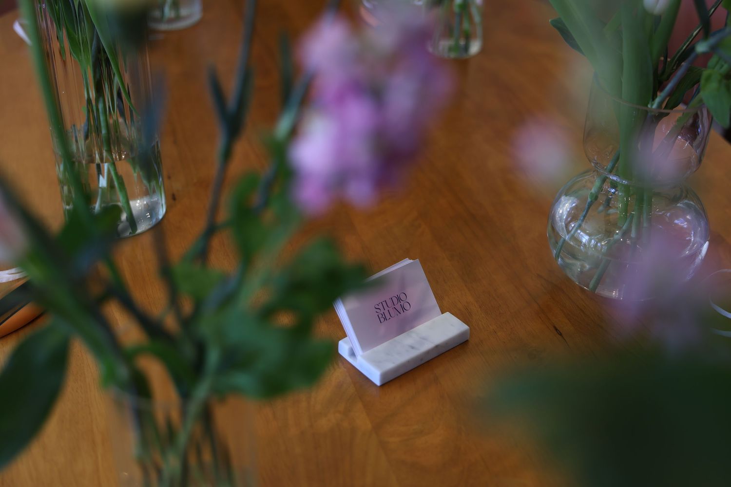 Elegant table setting with small place card holder surrounded by delicate pink floral arrangements in glass vases.