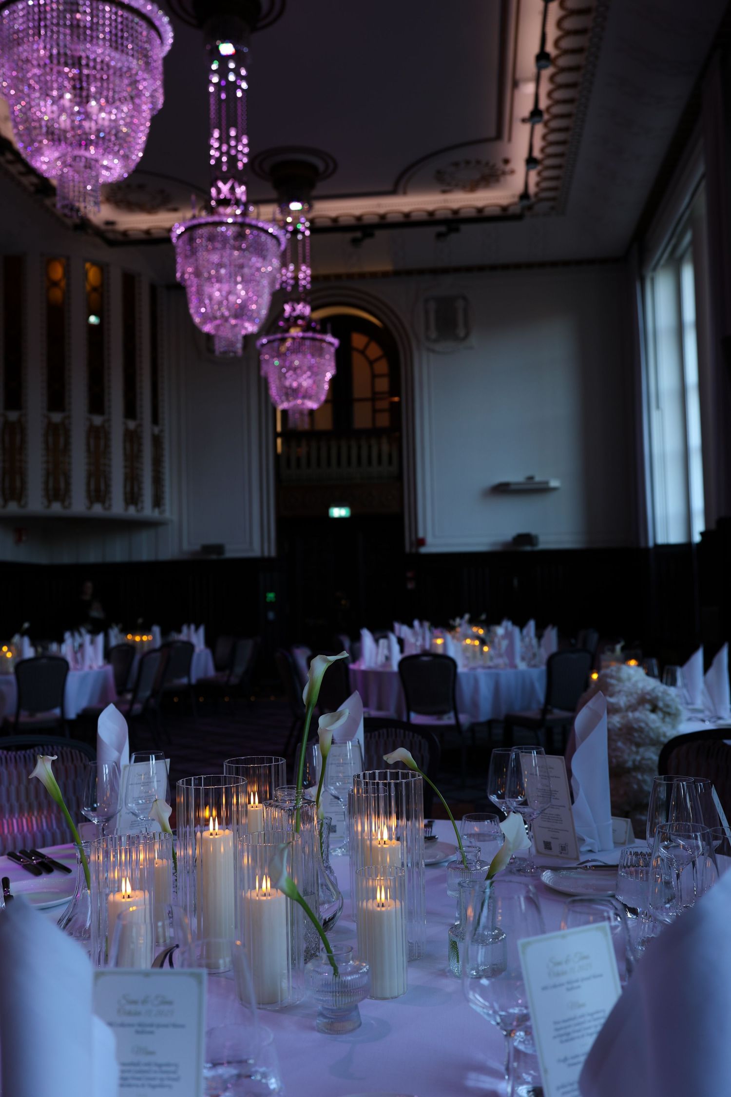 Elegant banquet hall with purple chandeliers, candlelit tables, white linens, and floral centerpieces for a formal dinner event.