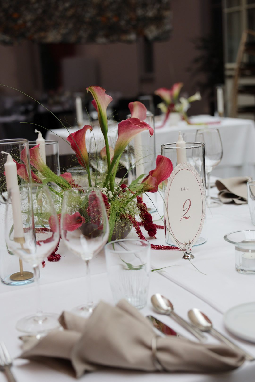 Elegant wedding reception table setting with pink calla lily centerpiece, table number 2, crystal glasses, and linen napkins.