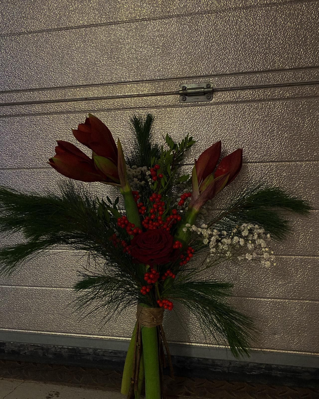 A winter floral arrangement with red amaryllis blooms, pine branches, red berries and white flowers tied in a bouquet.