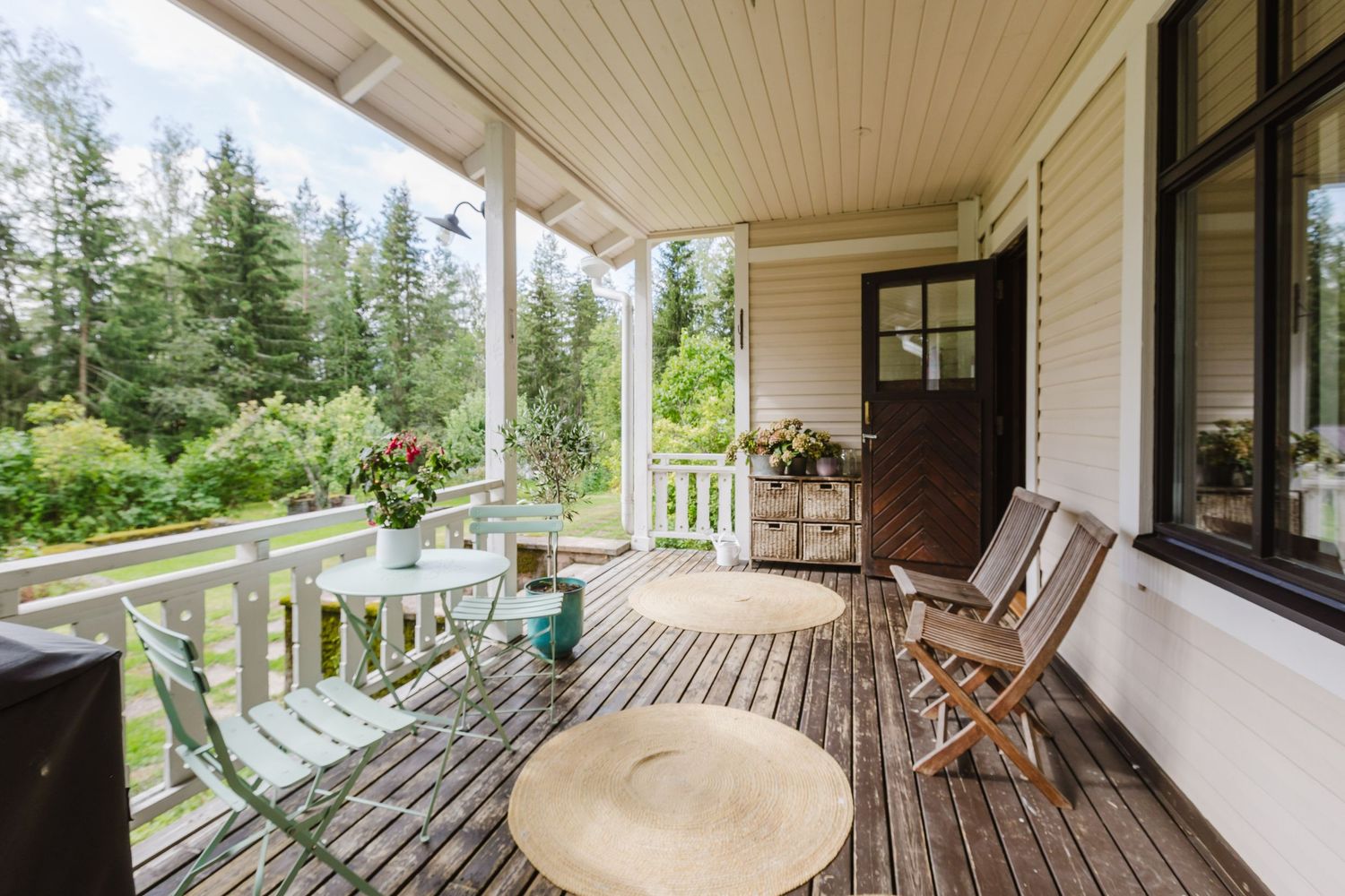 Charming wooden porch with bistro table, folding chairs, and lush forest views on a sunny day.