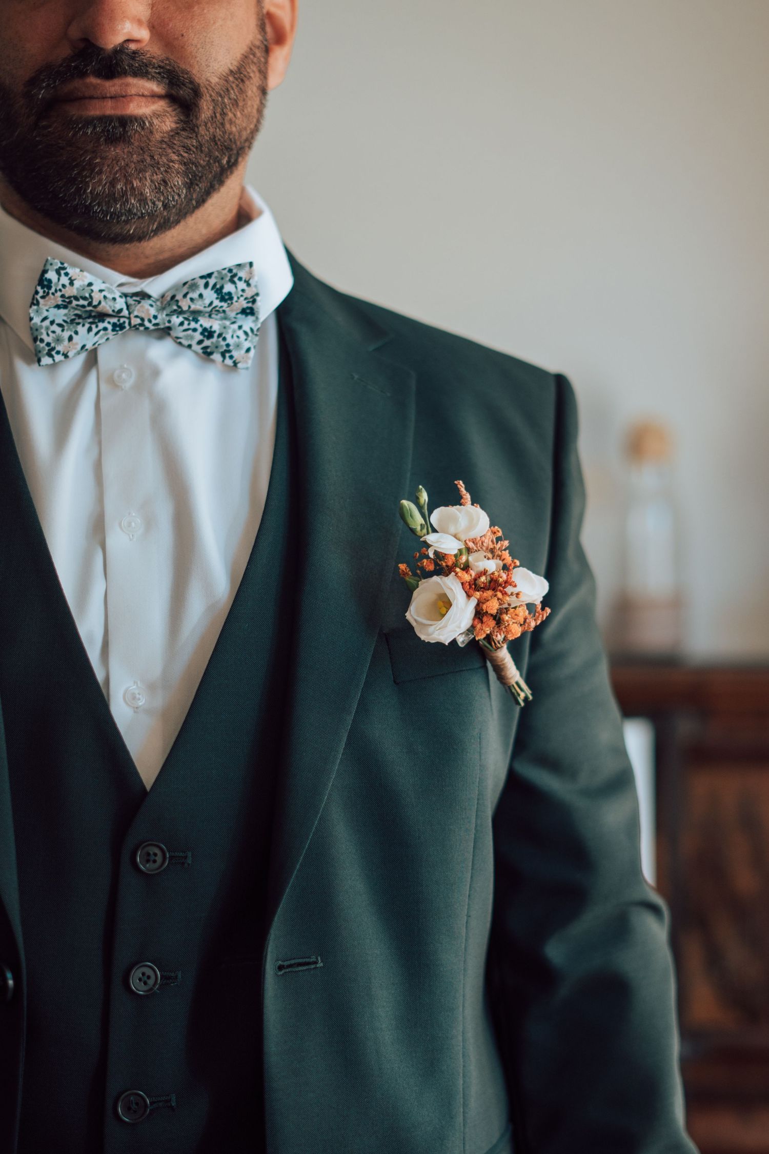 Groom in dark green suit with floral boutonniere and patterned bow tie on wedding day.