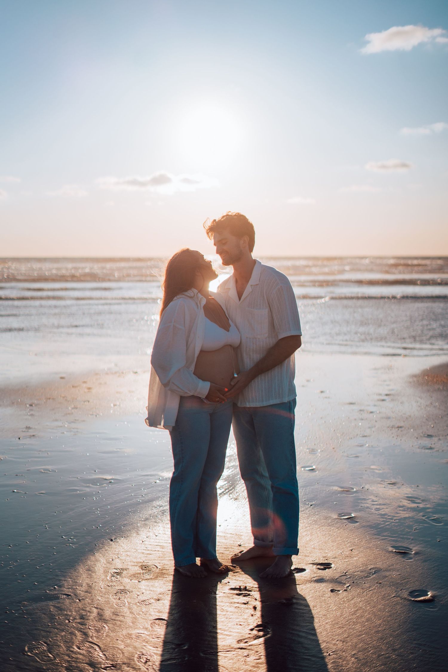 Couple holding hands and gazing at each other on a reflective beach at golden hour sunset.