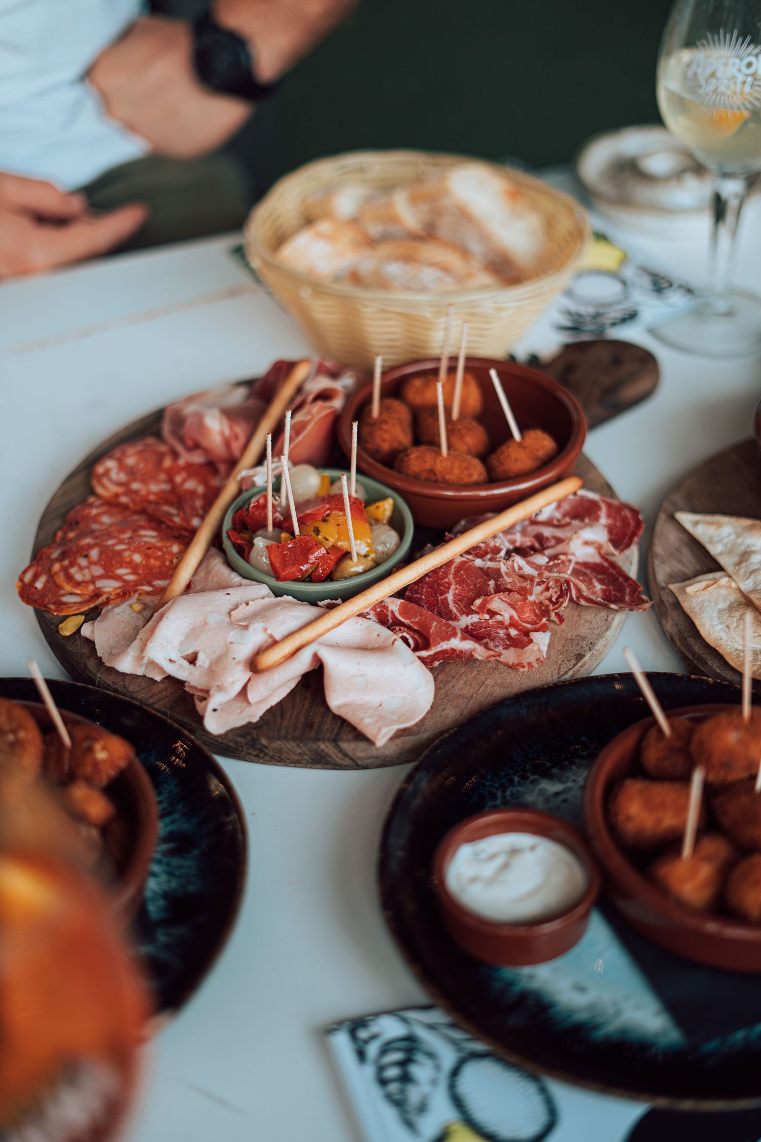 Rustic charcuterie board with cured meats, appetizers, and wine on white table.