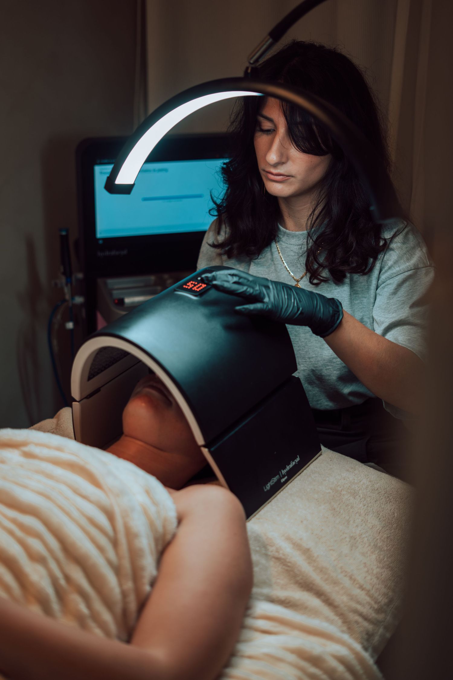 Esthetician in black gloves performing LED light therapy treatment on client in professional beauty salon.